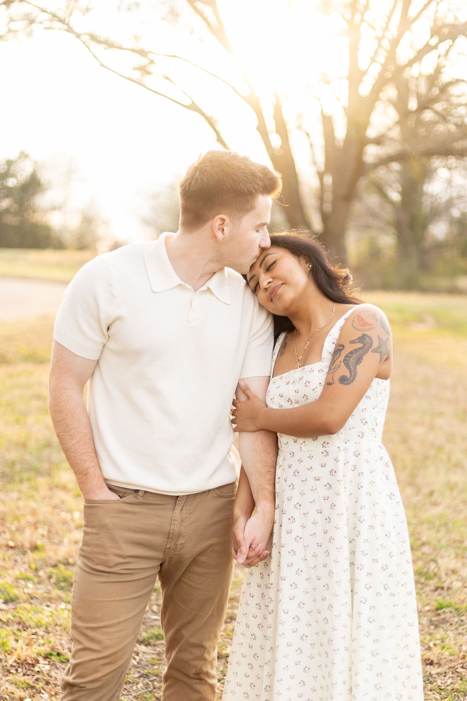 Romantic couple embracing outdoors during golden hour in casual white and tan outfits.