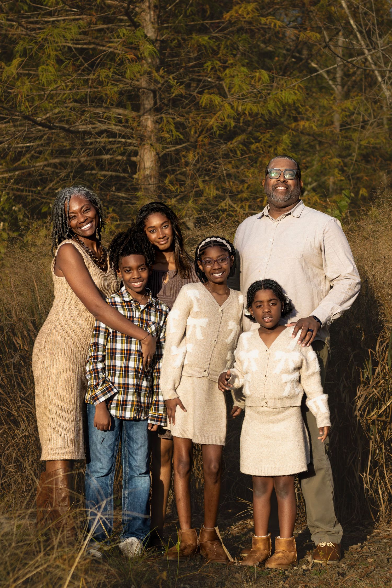 A family group portrait taken outdoors with autumn trees in the background.