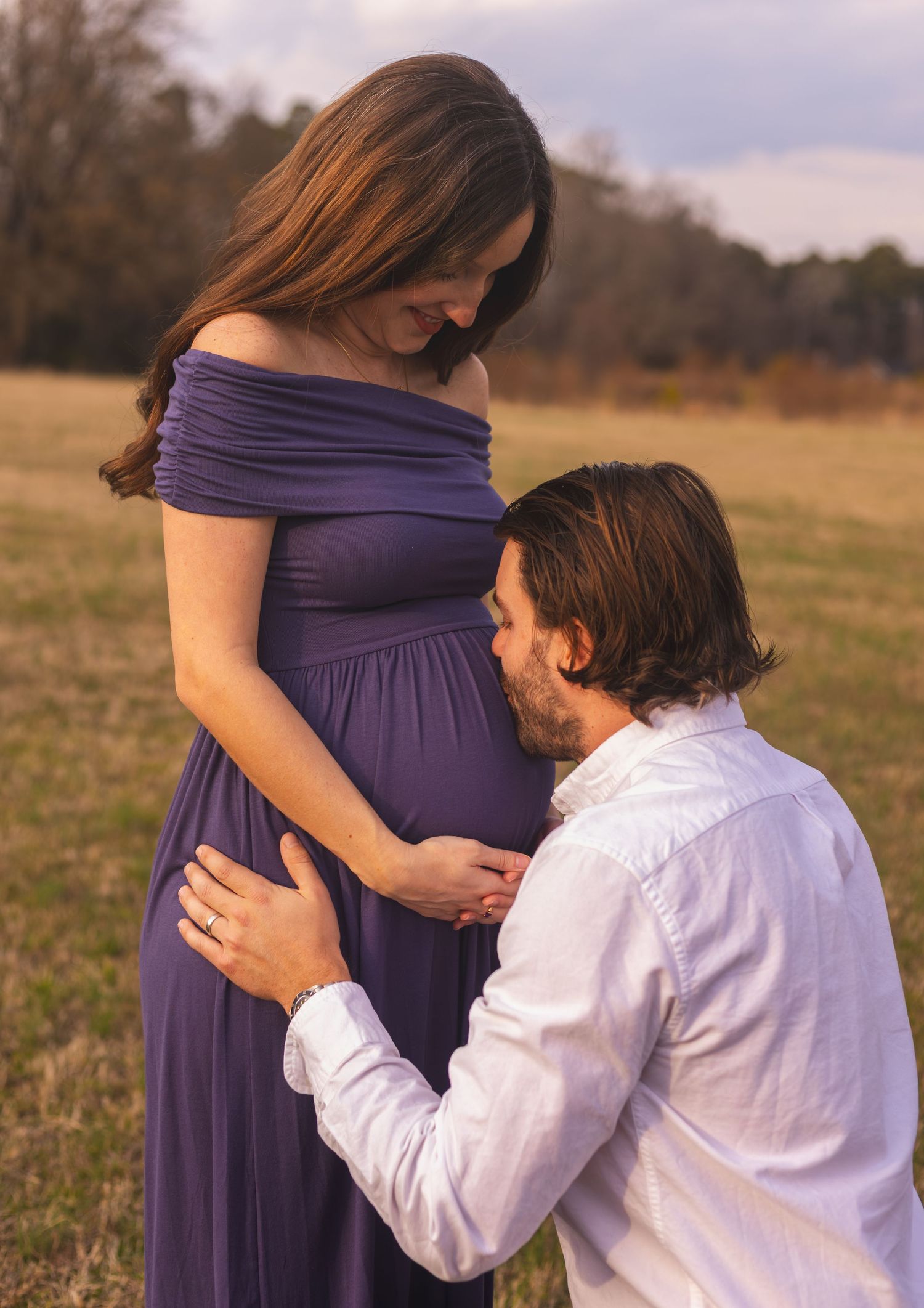 Maternity photo series showing tender moments between couple in field at sunset.