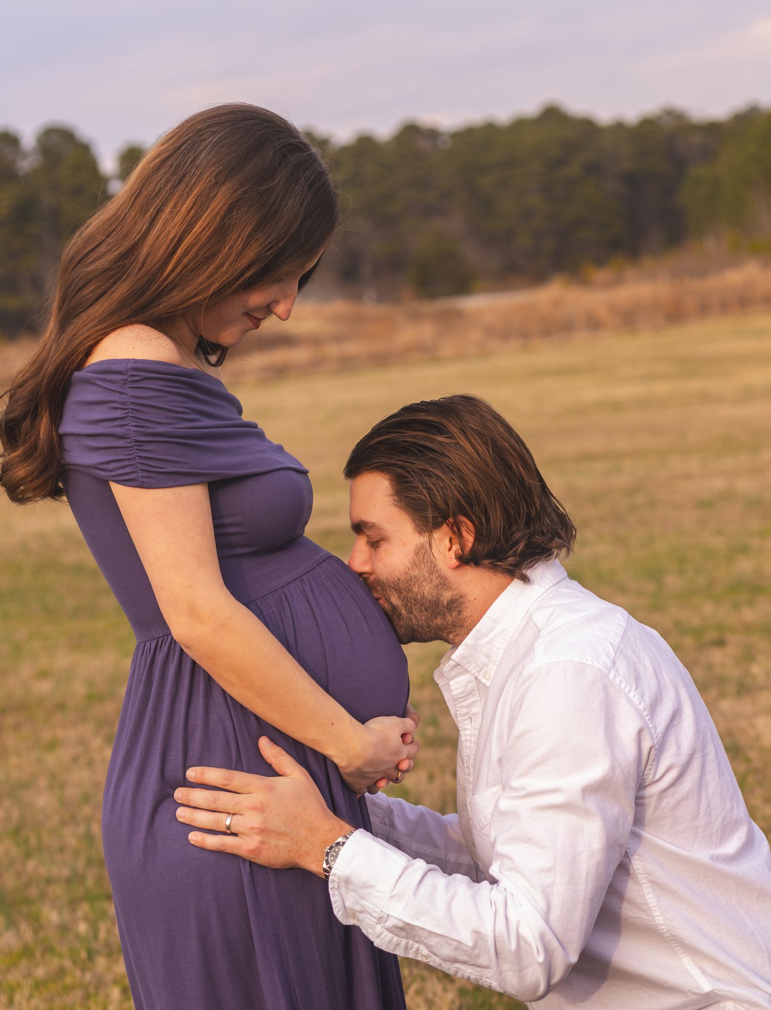 Intimate maternity photo session with couple in a field at sunset.