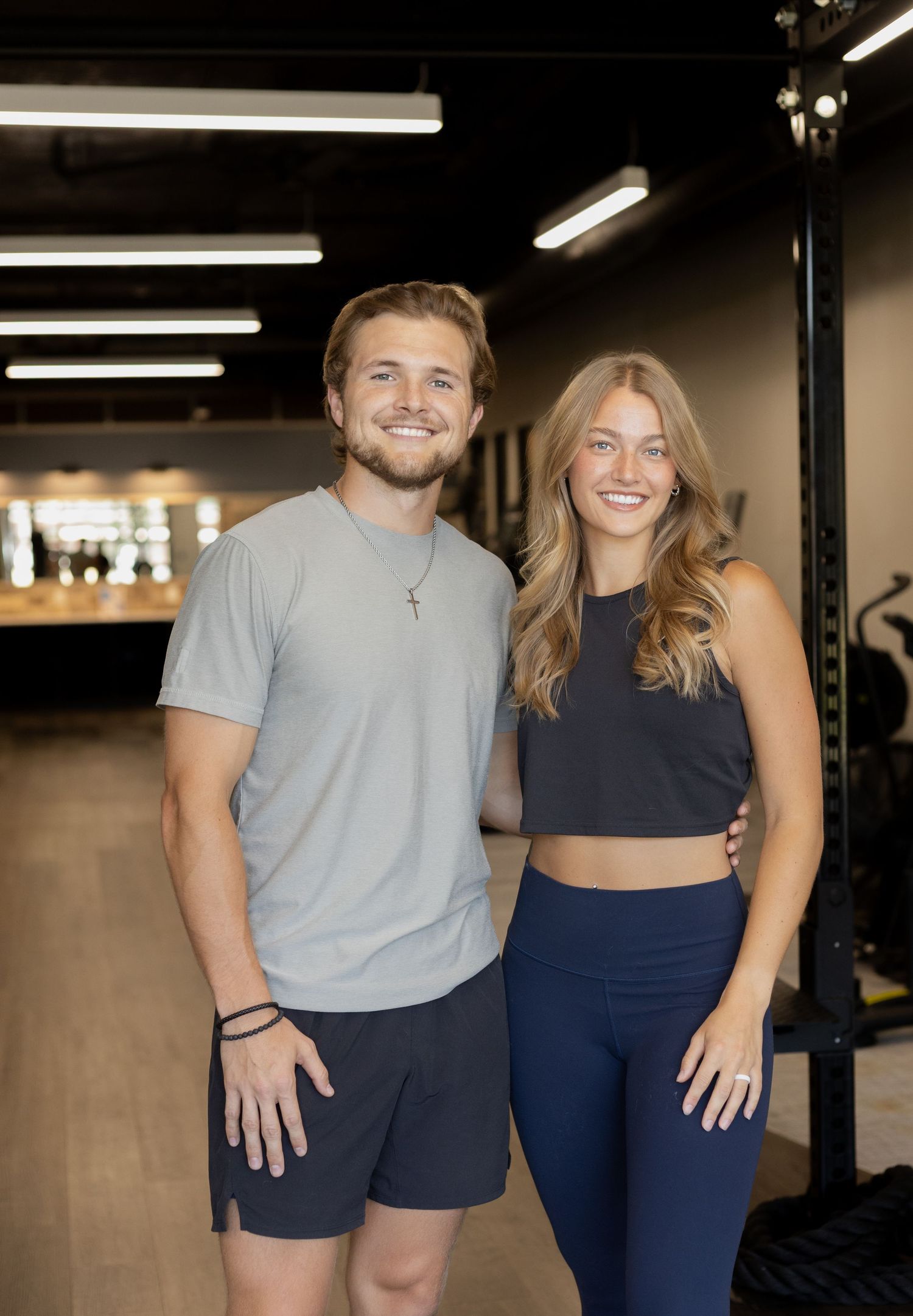A smiling man and woman in athletic wear pose together in a modern gym fitness center.