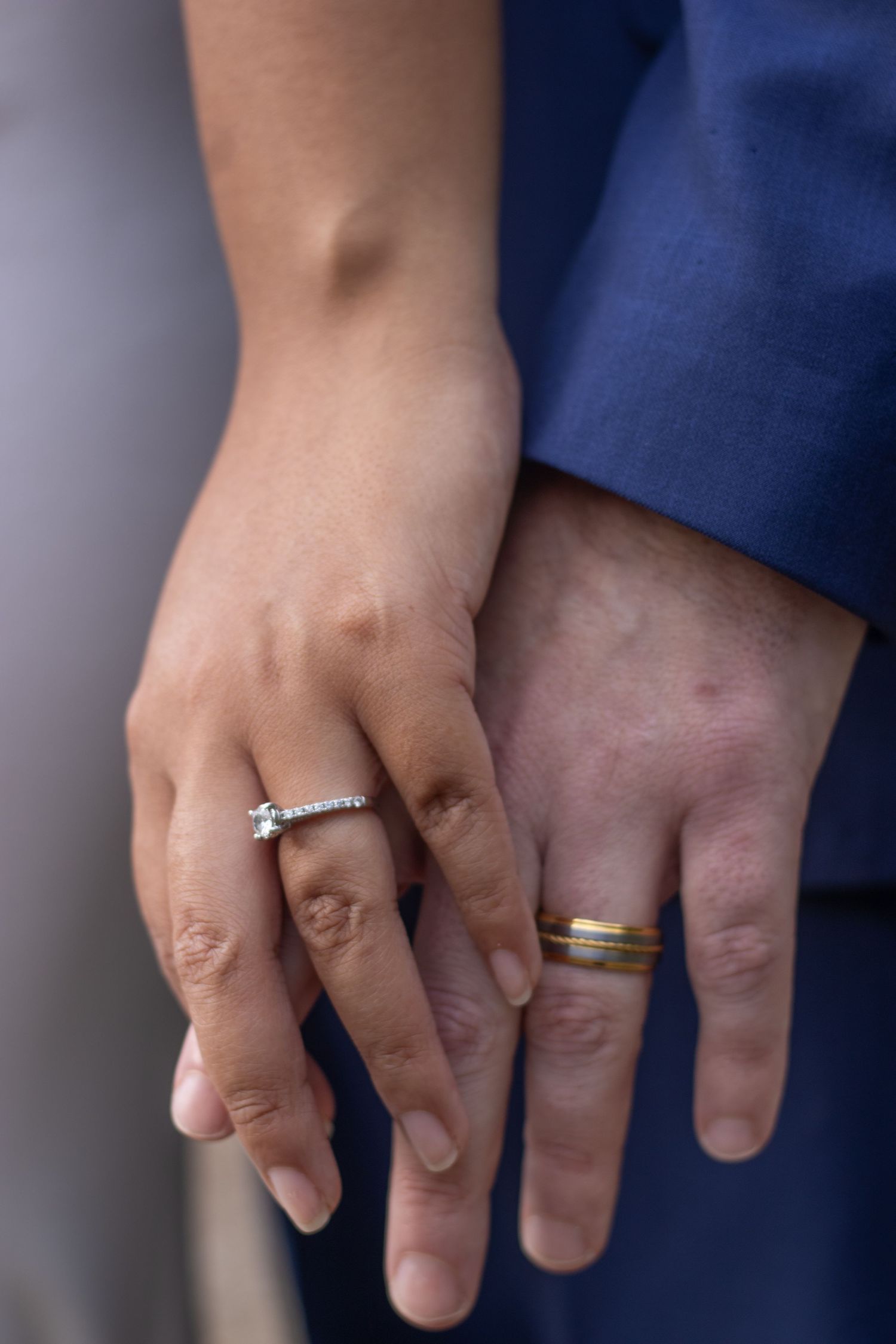 Close-up shot of two hands wearing wedding rings against a dark background.