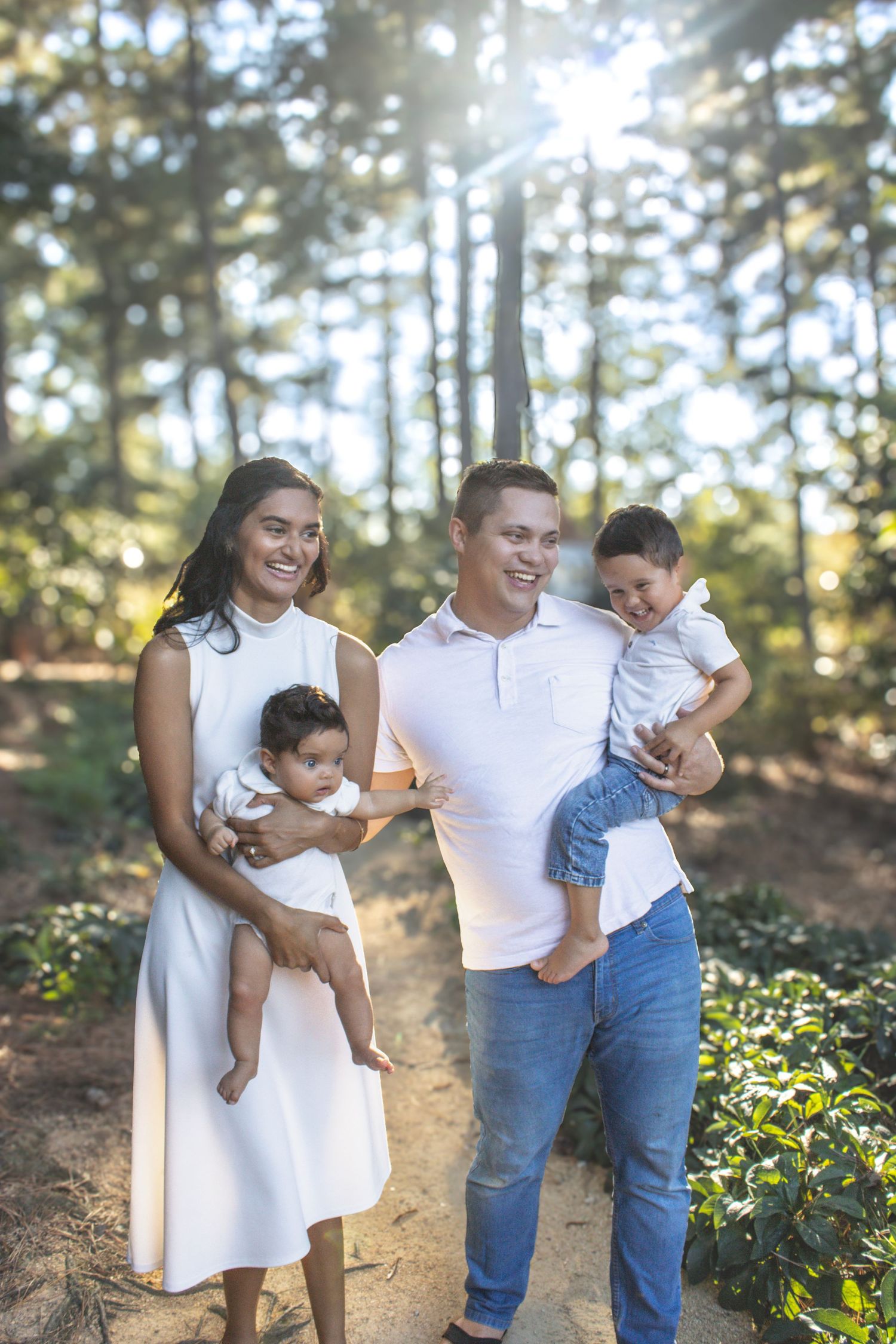 Family photo session in sunlit forest wearing coordinated white and denim outfits.
