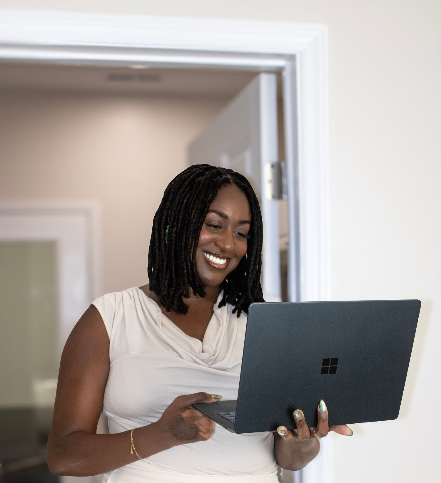Professional working on Surface laptop while smiling in bright office setting.