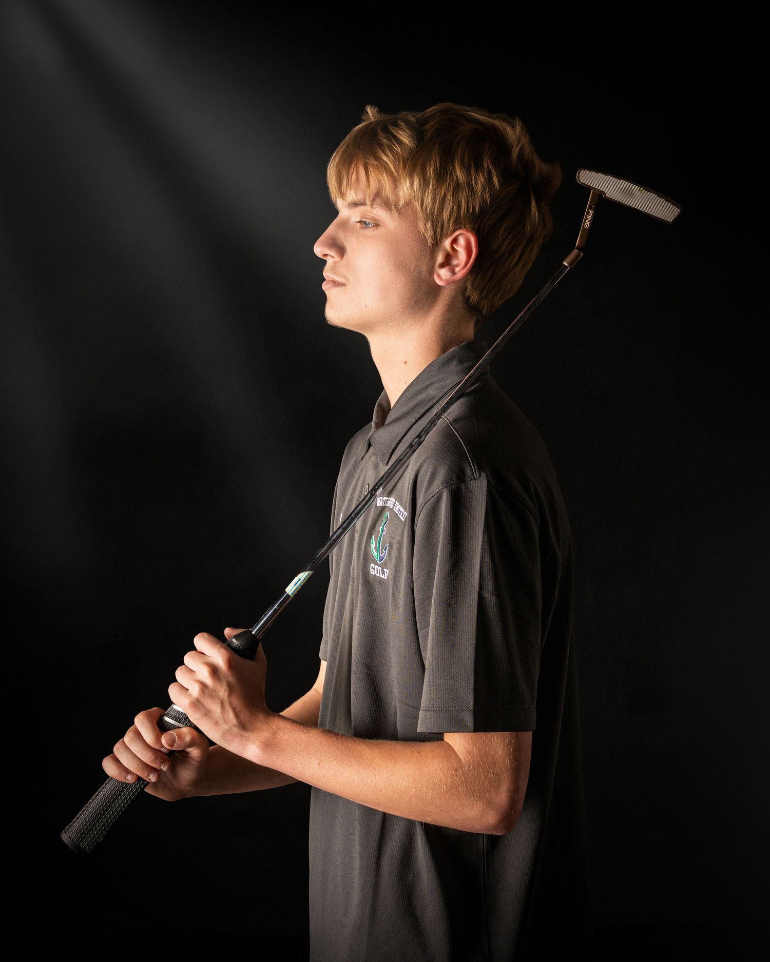 Young male golfer holding a golf club over his shoulder, posing dramatically against a dark background.