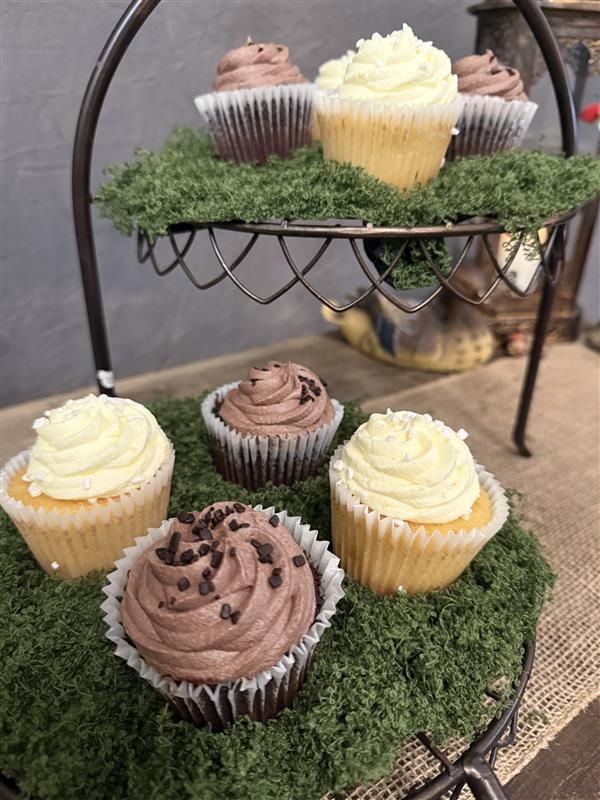 Chocolate and vanilla cupcakes with frosting displayed on a two-tier metal stand decorated with artificial grass.