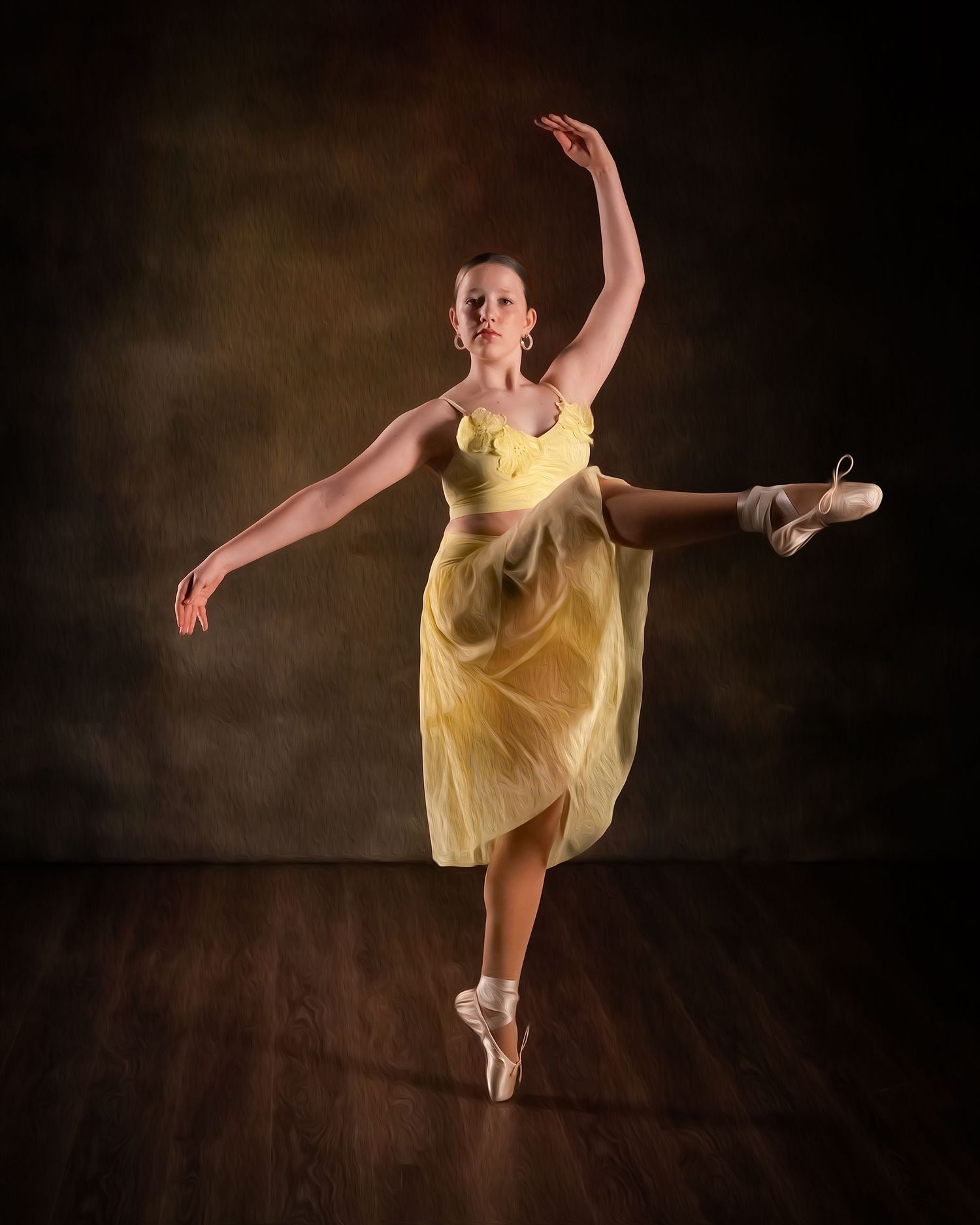 A ballerina in a yellow dress performs an arabesque on pointe shoes against a dark studio backdrop.