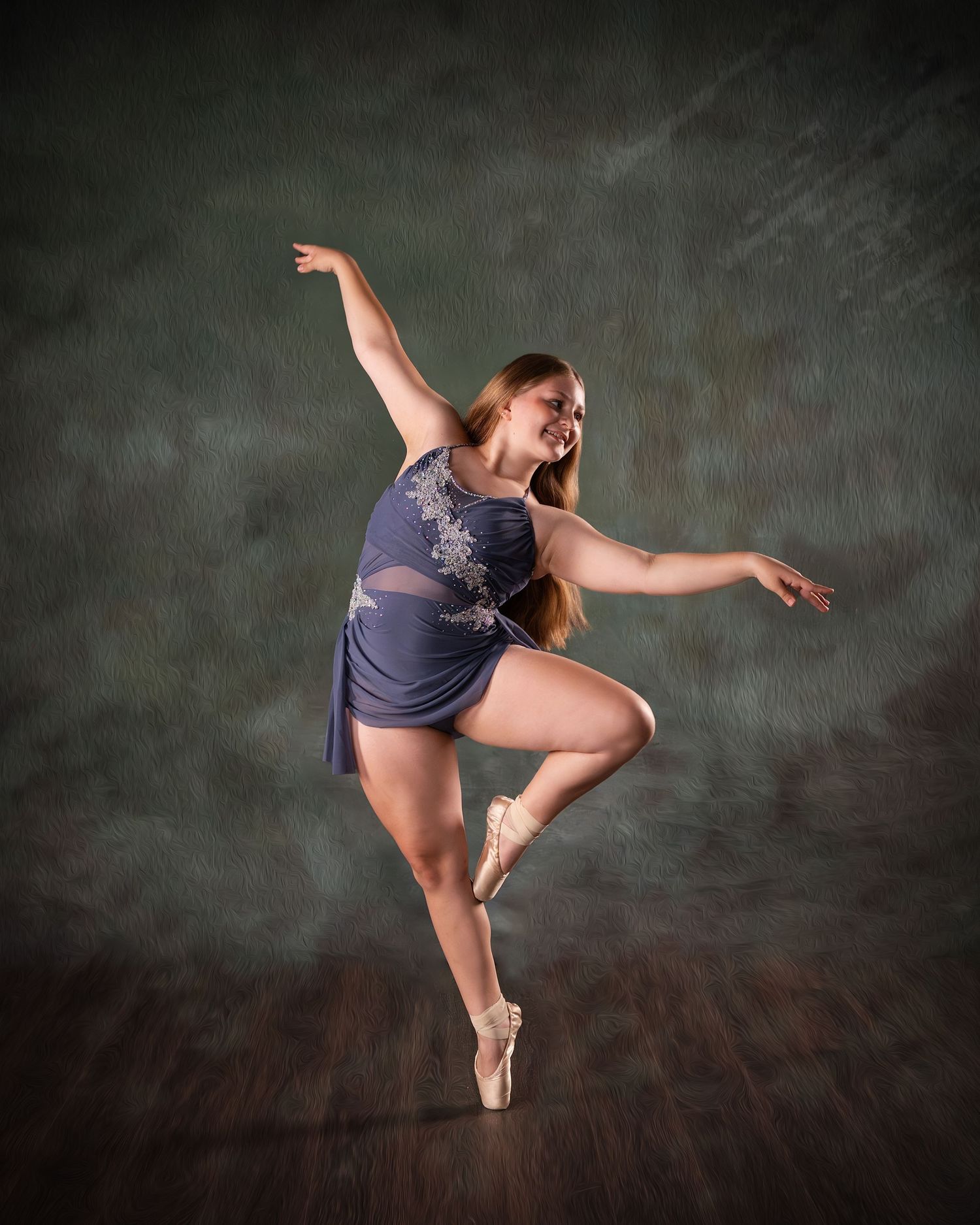 A graceful ballet dancer in a blue dress performs an arabesque on pointe shoes against a dark studio backdrop.