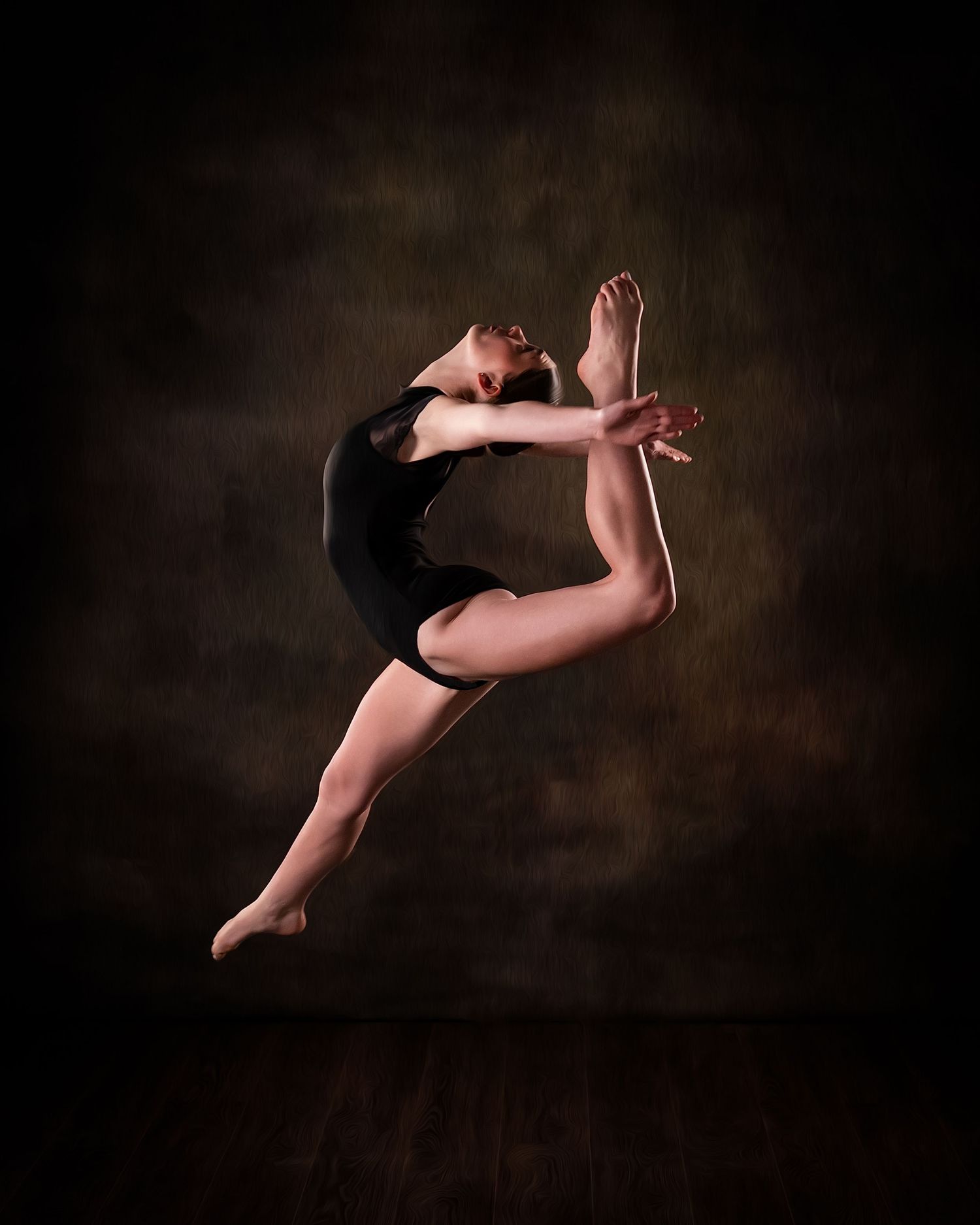 A ballet dancer in a black leotard performs a graceful leap against a dark studio backdrop.