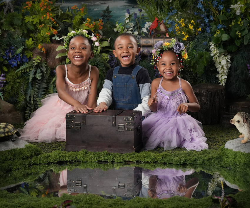 Three young children in floral crowns and colorful tutus posing in an enchanted forest studio.