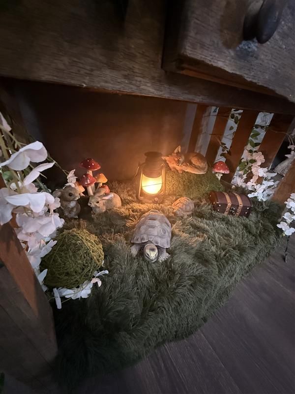 Nativity scene with illuminated stable, figurines of Mary, Joseph, baby Jesus, animals, and shepherds surrounded by evergreen branches.
