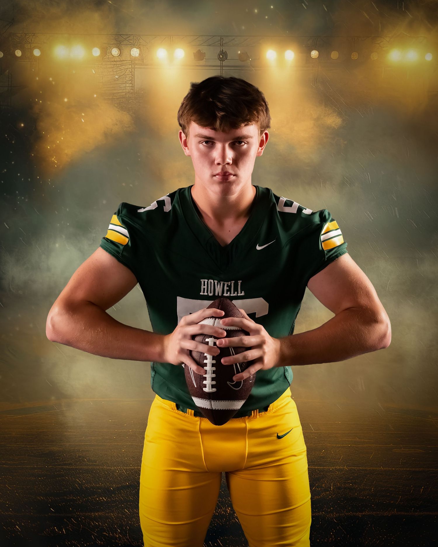 Young football player in Howell green jersey and yellow pants poses with football under stadium lights.