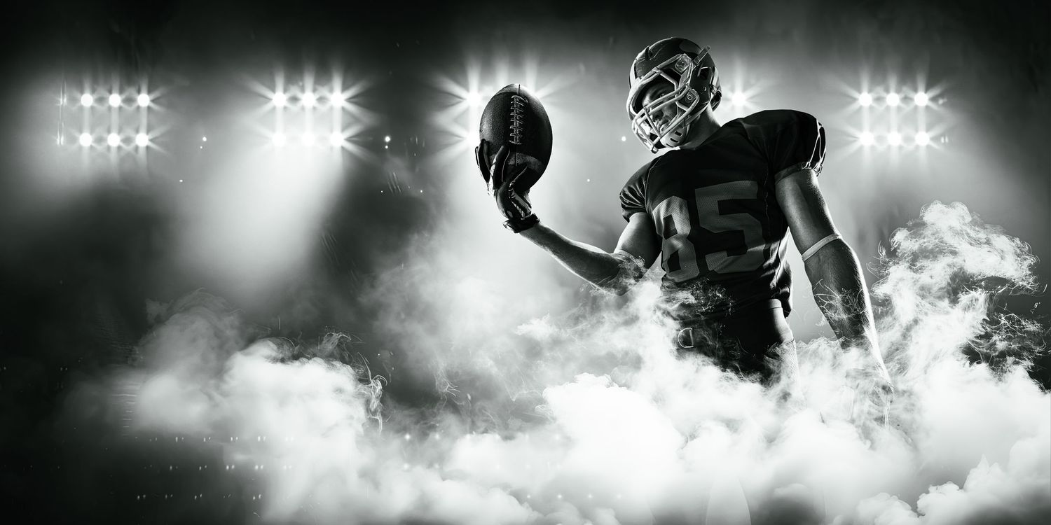 Black and white photo of an American football player holding a ball under dramatic stadium lights with smoke effects.