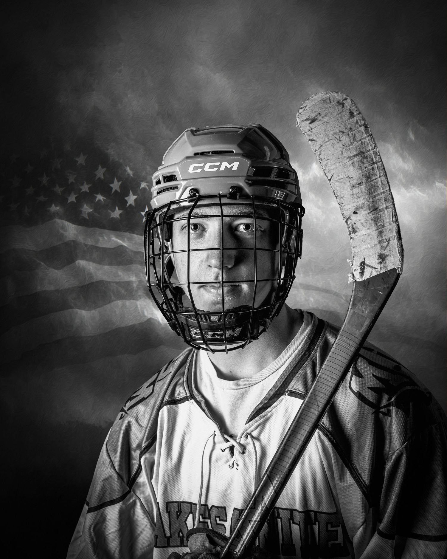 Black and white portrait of a young hockey player in CCM helmet and jersey, holding a stick with American flag backdrop.