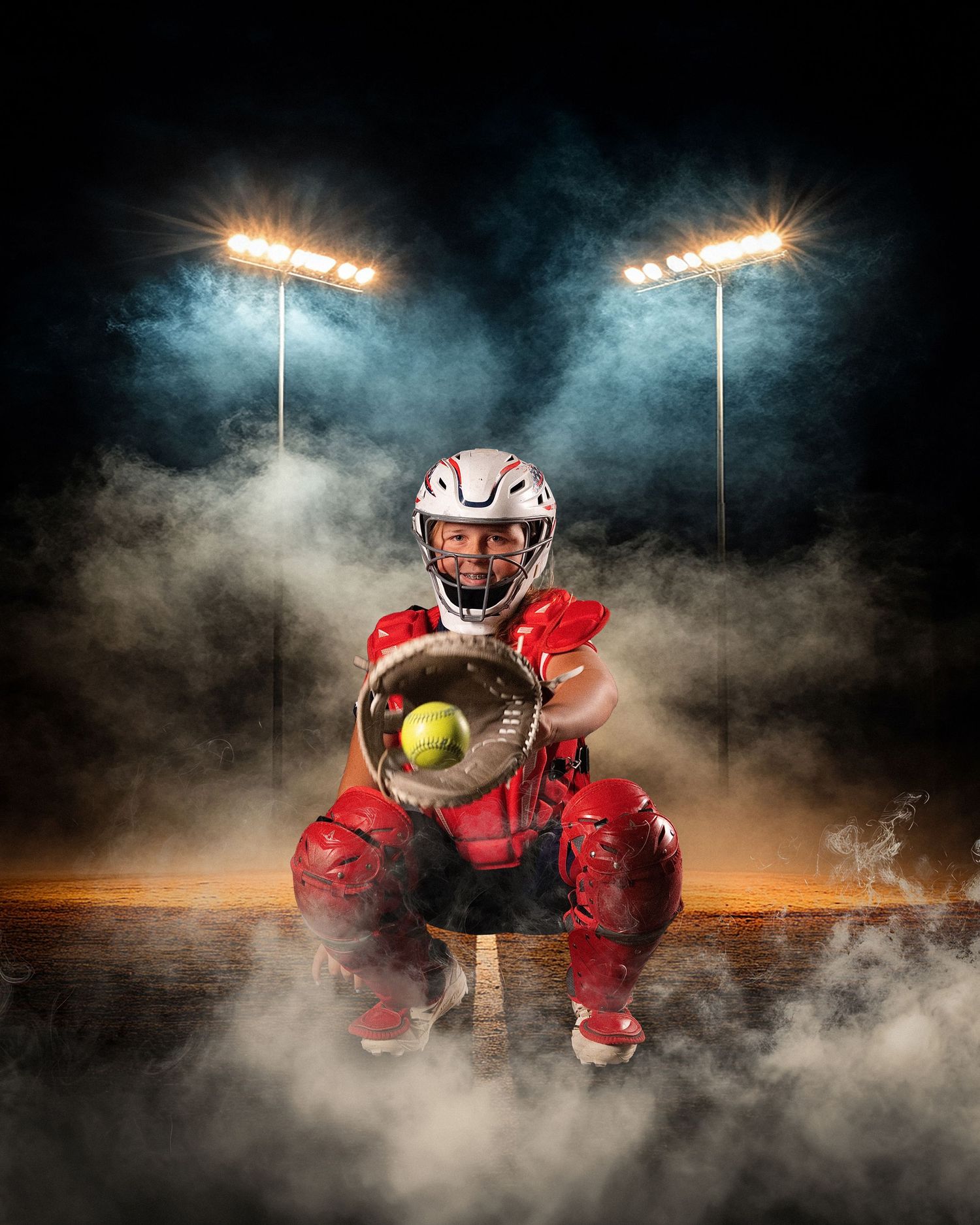 A softball catcher in red gear crouches dramatically under stadium lights surrounded by atmospheric smoke.