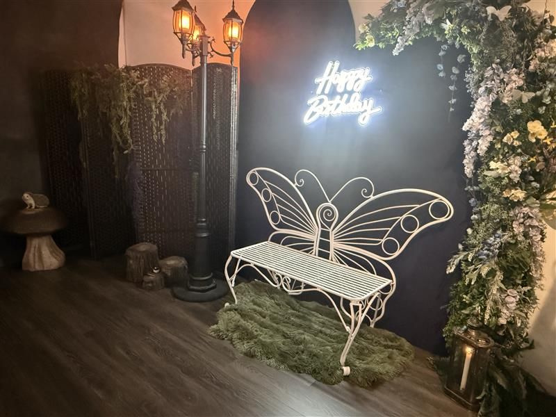 Elegant birthday party setup with neon 'Happy Birthday' sign, white butterfly bench, floral arrangements, and decorative lighting.