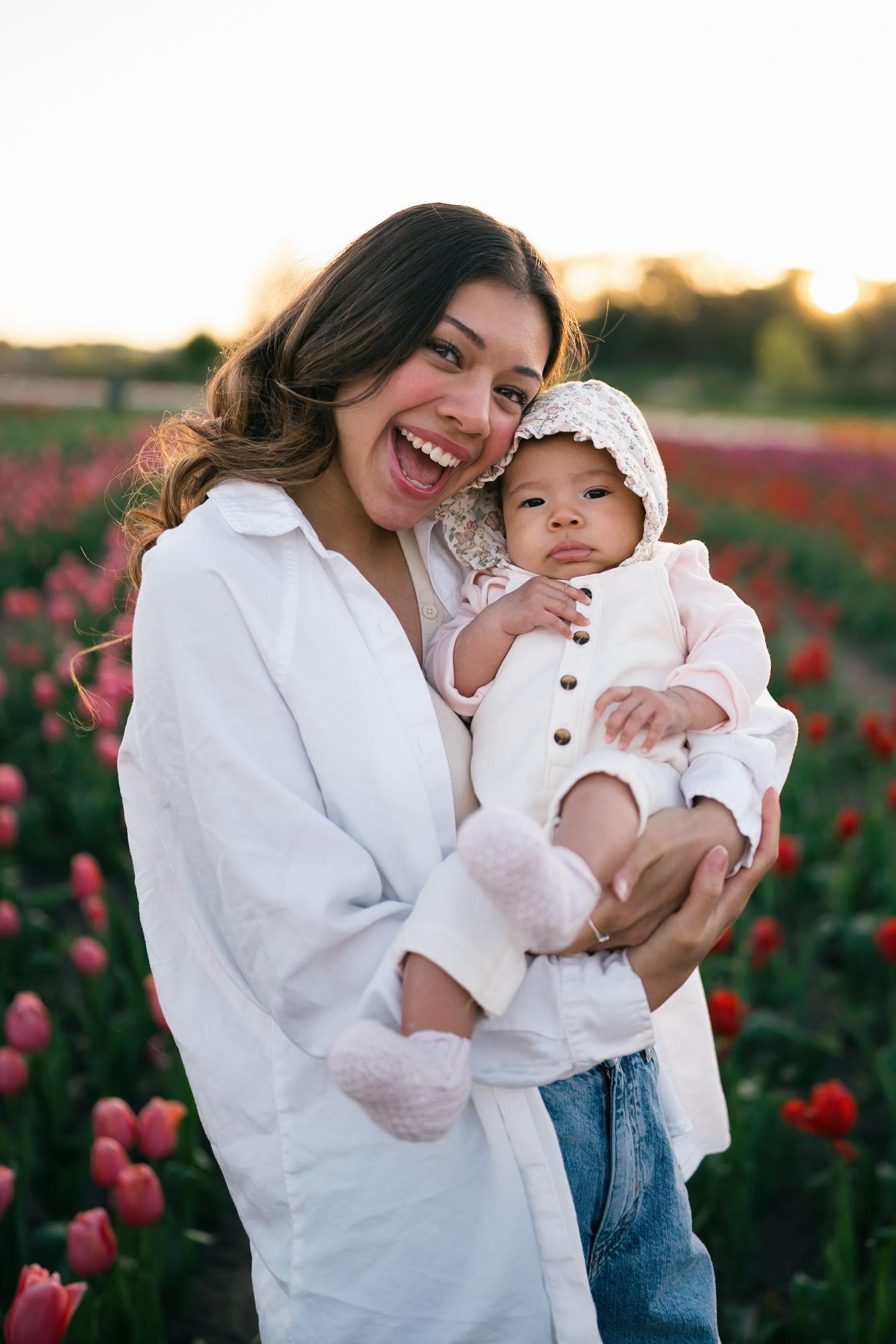A joyful moment captured in a tulip field with parent and baby in matching white outfits.