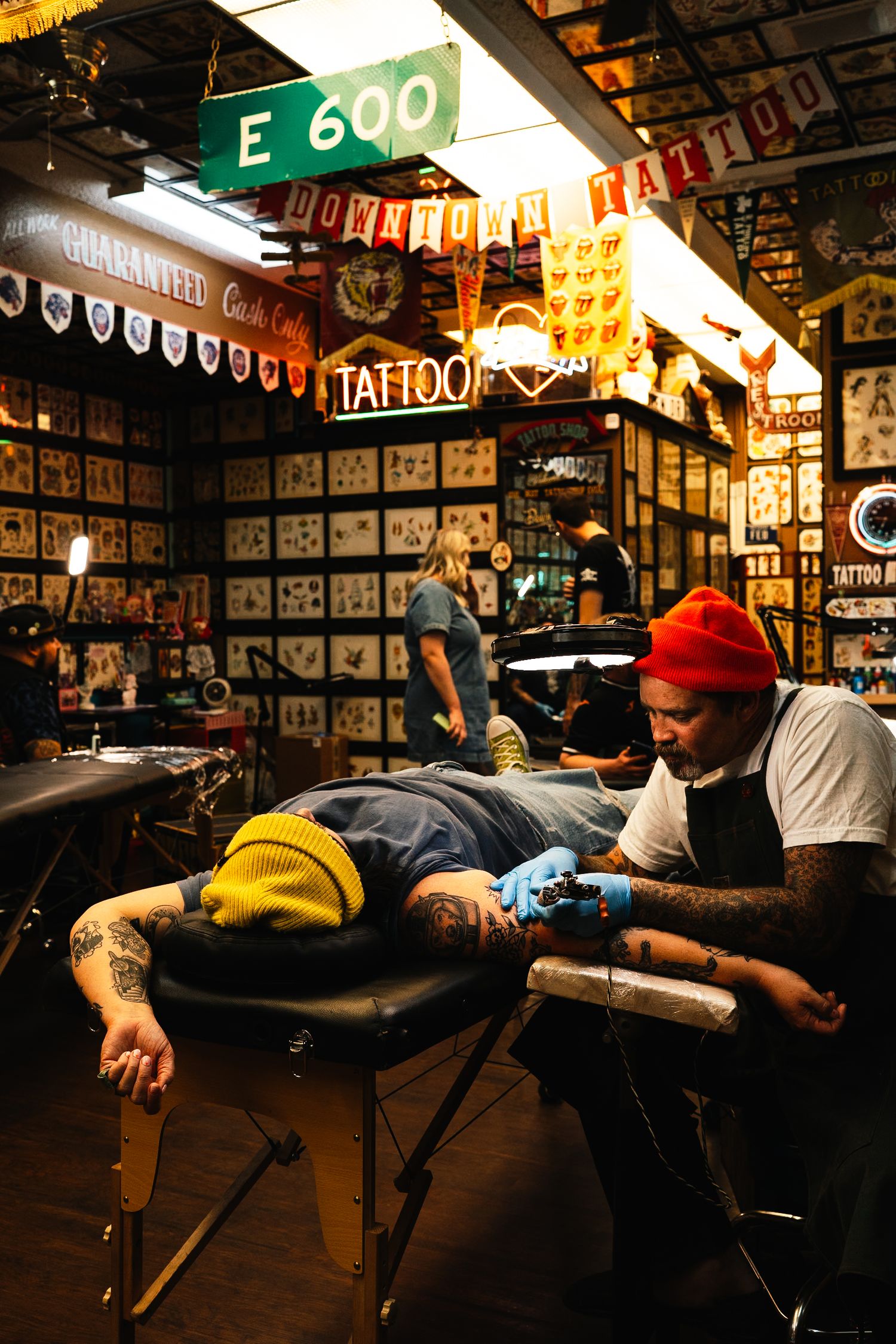 Tattoo artist working on client in shop decorated with classic flash art and banners.