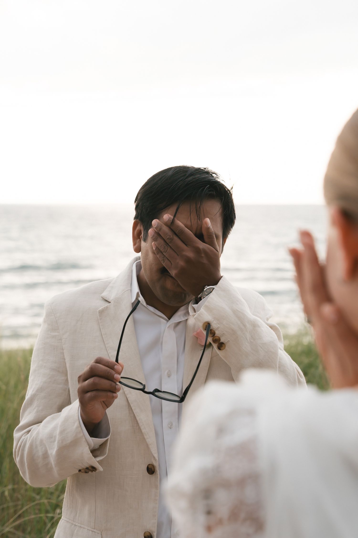 Wedding guest in white suit showing emotional reactions during outdoor ceremony.