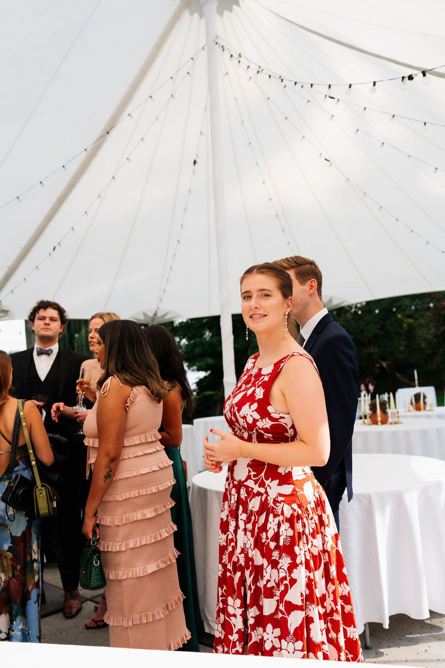Wedding guests mingling under a white tent with string lights during a reception celebration.