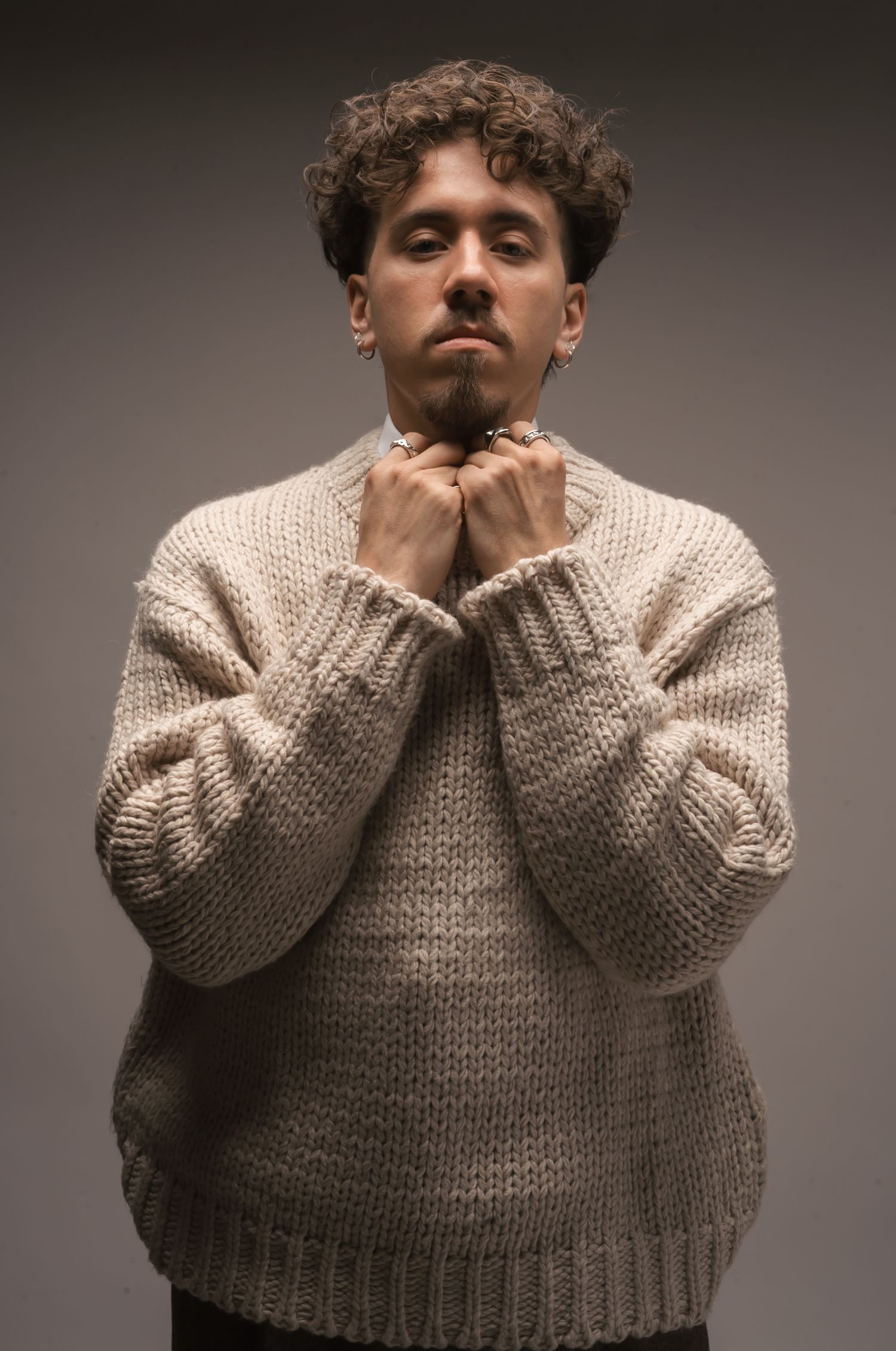 Model showcases cozy beige knit sweater in dramatic studio photoshoot sequence.