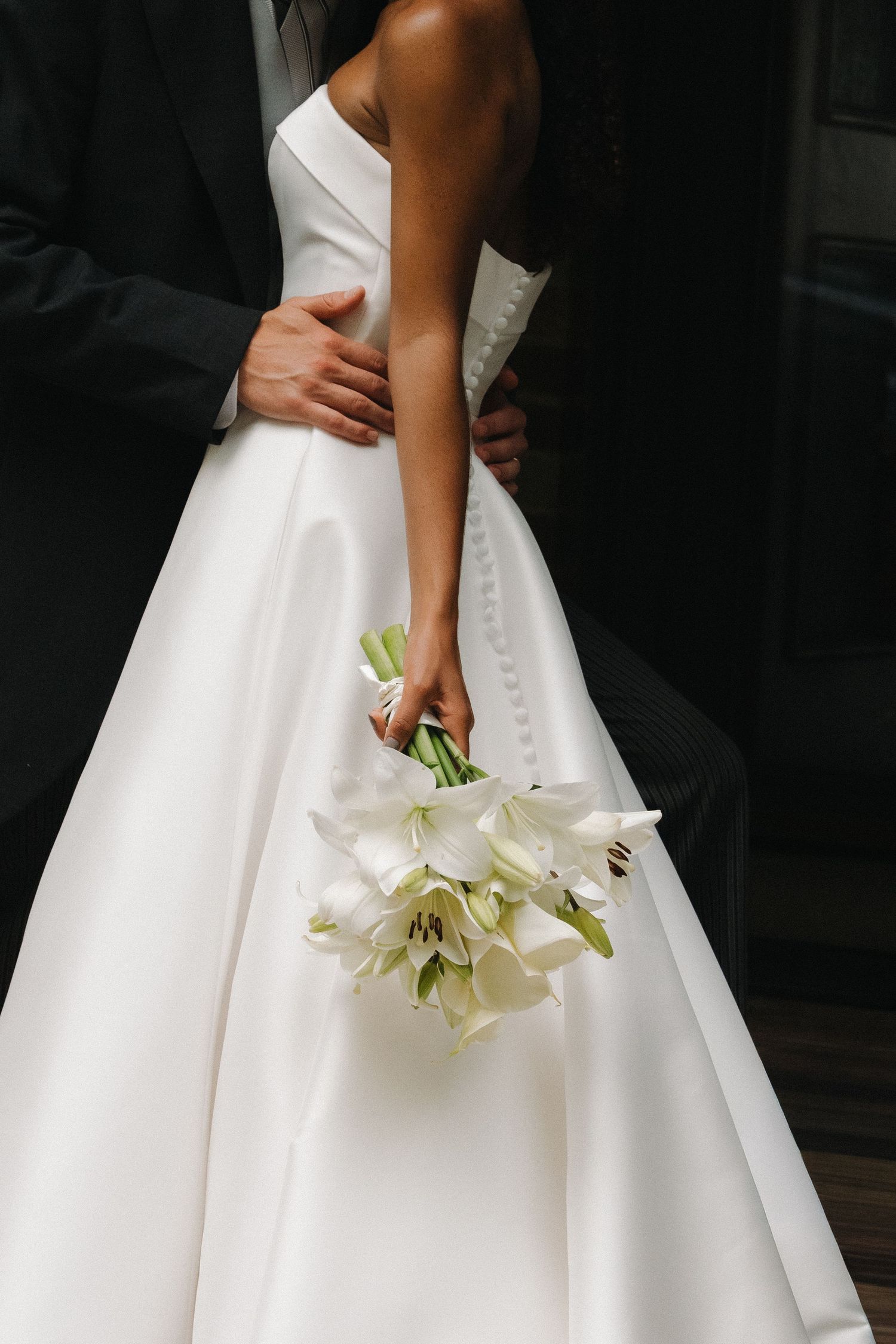 Elegant white wedding dress detail with cascading white lily bouquet.