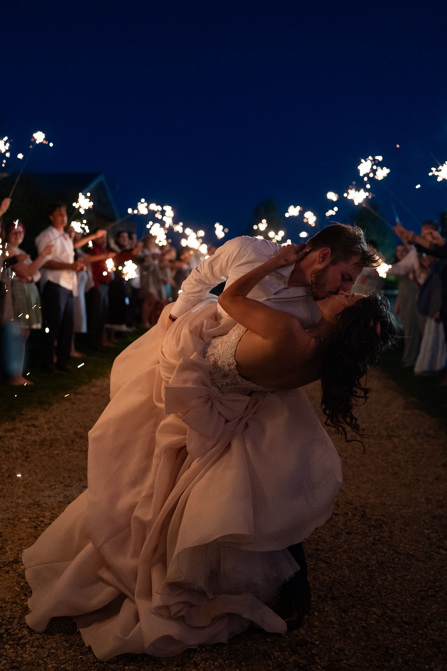 A bride in a flowing white dress dips dramatically under a sparkler-lit night sky.