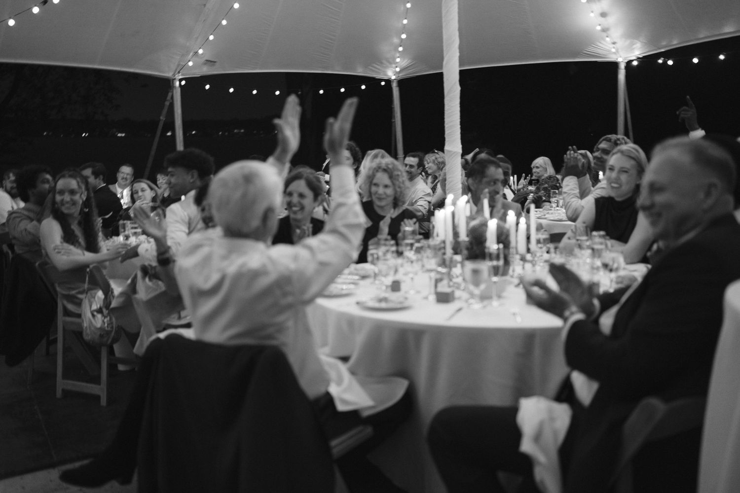 Wedding reception dinner under tent with guests seated at round tables.