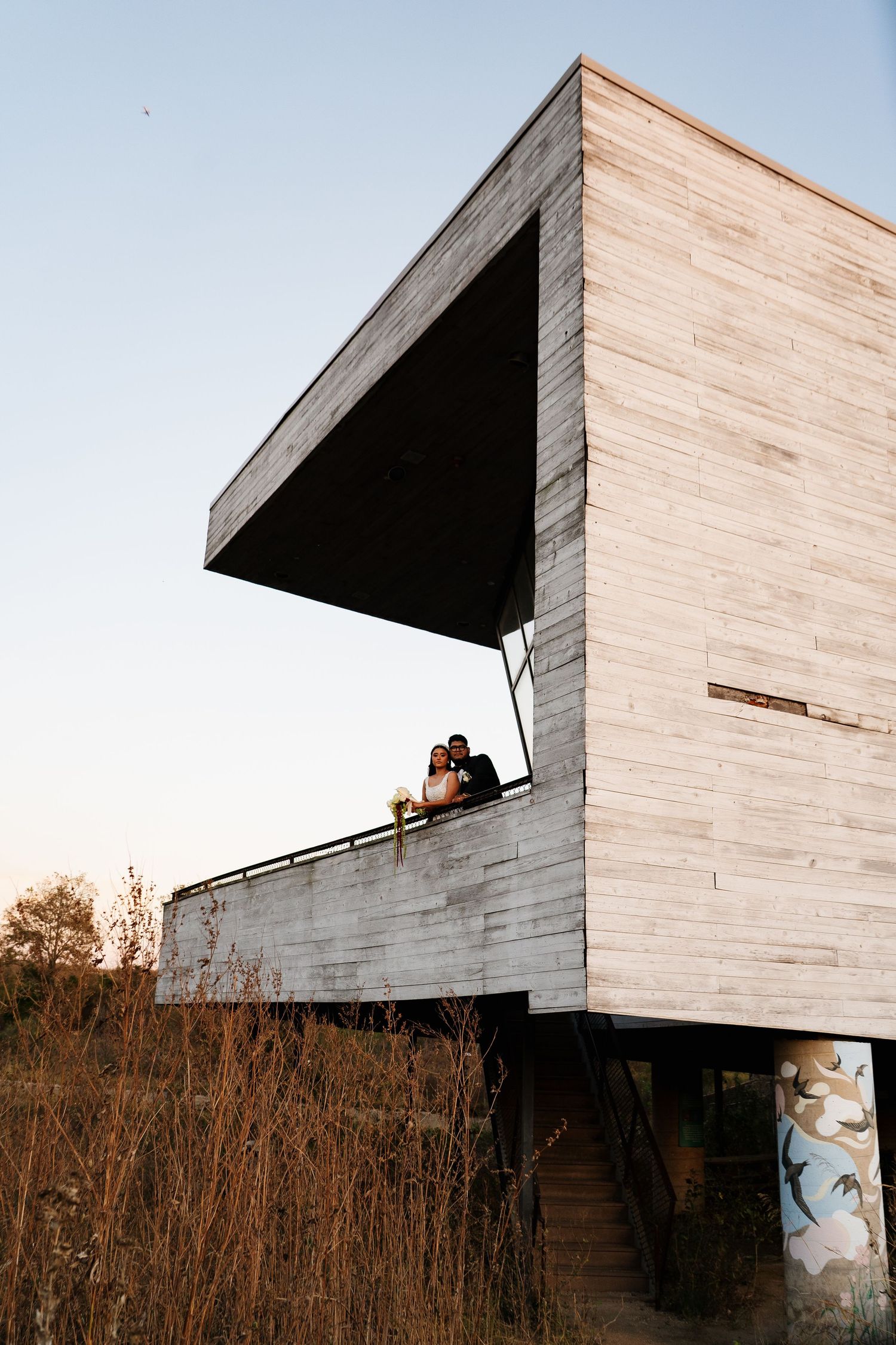 Modern concrete building with angular architecture and overhanging sections against a sunset sky.