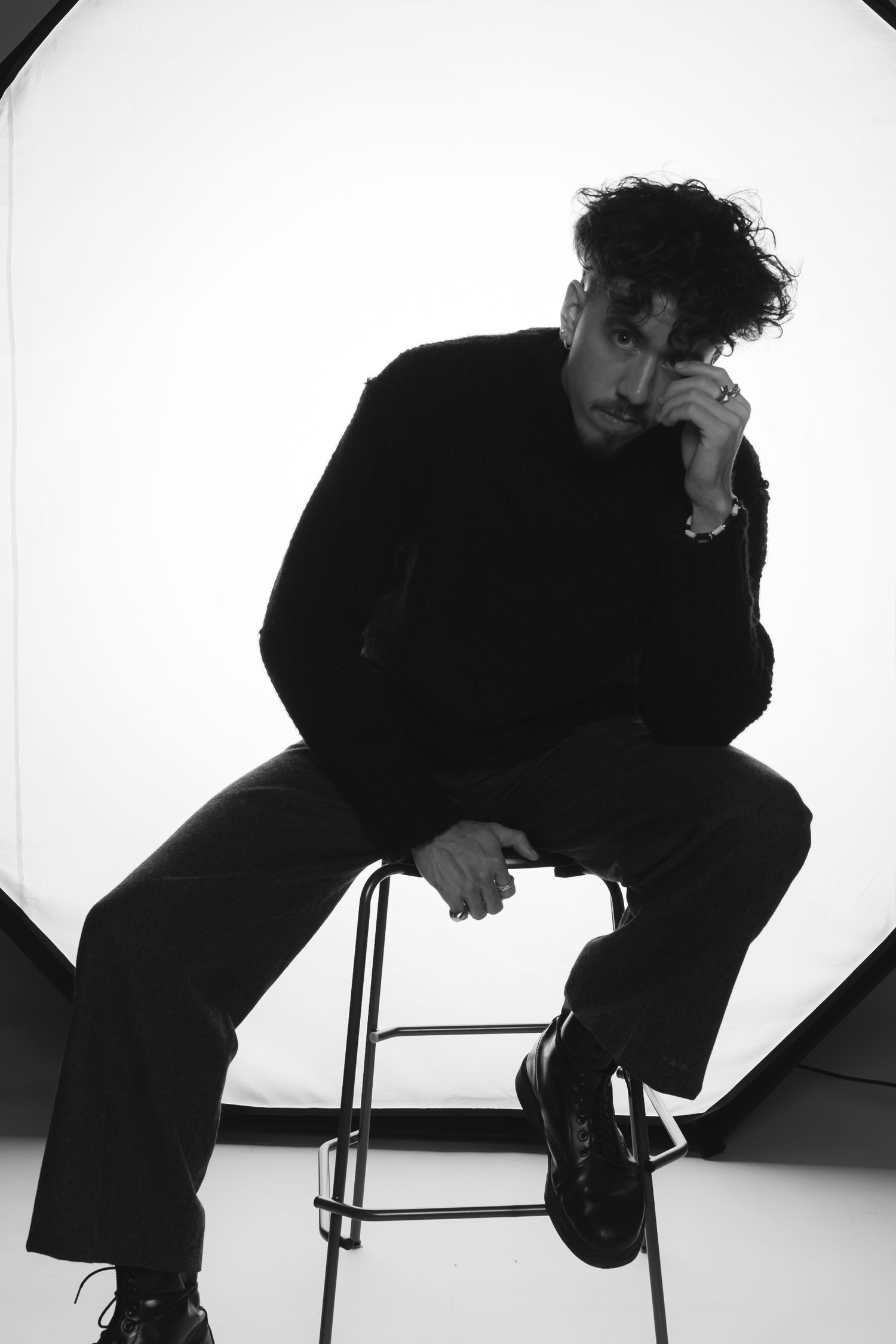 Silhouetted figure in dark clothing poses on chair in artistic black and white studio shots.