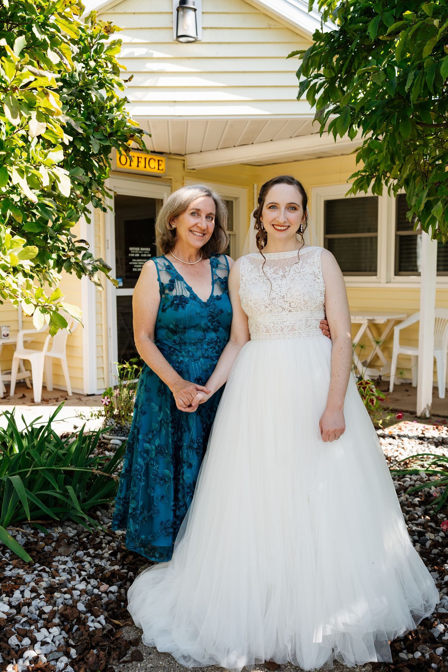 Wedding day portrait outside yellow house with white and teal dresses.
