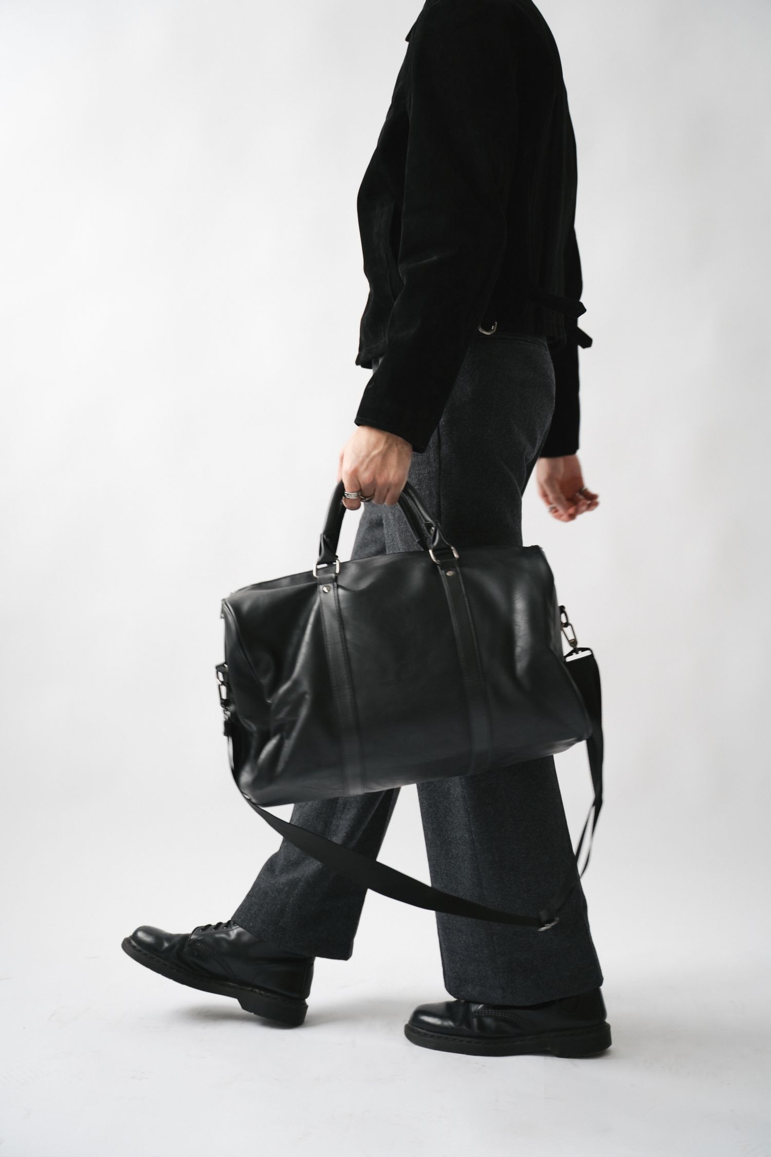 Close-up of black shoes and bag in motion against white studio backdrop.