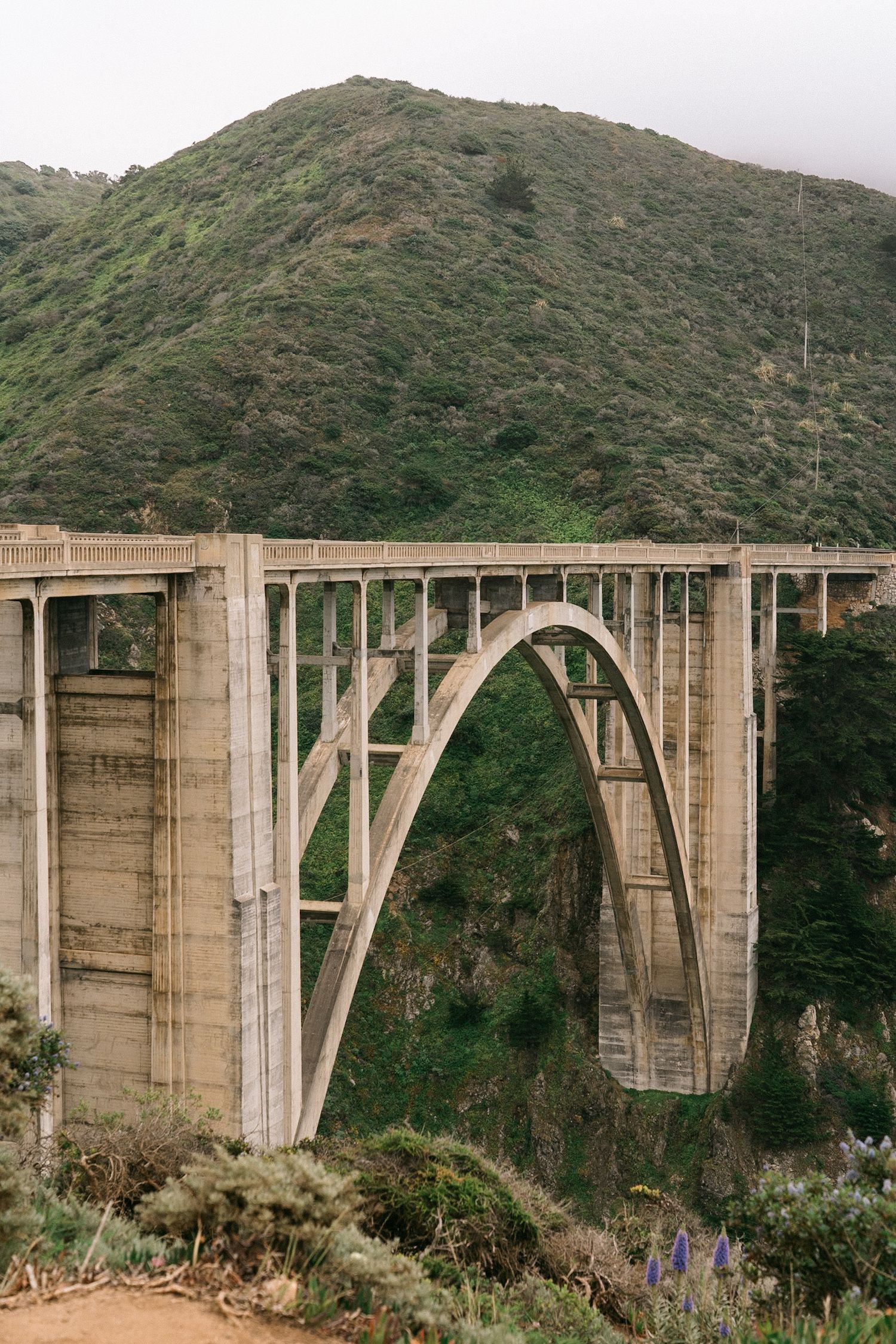 A concrete arch bridge spans across a mountainous valley in dramatic landscape.