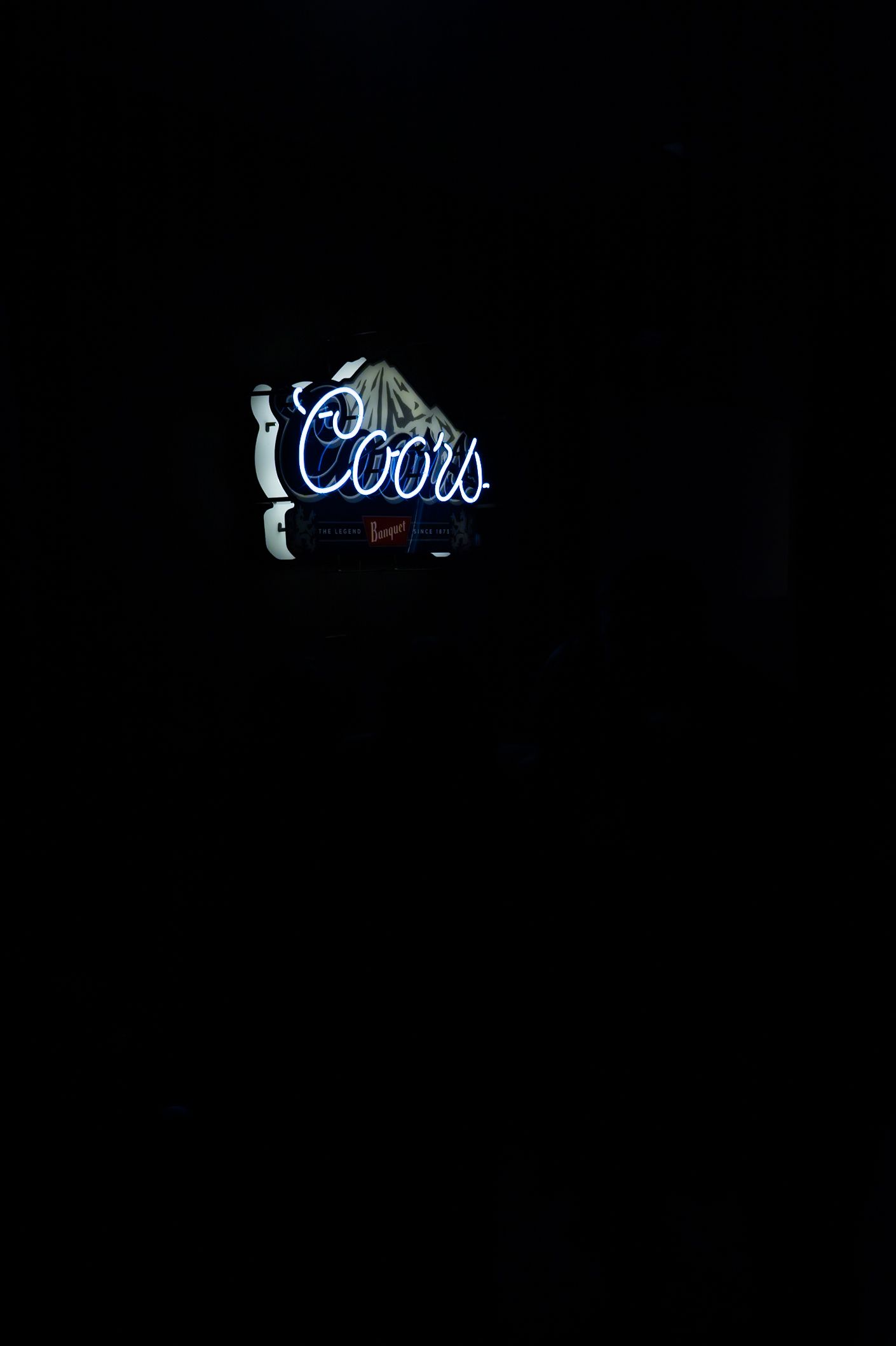 Glowing blue Coors neon sign illuminated against dark background.