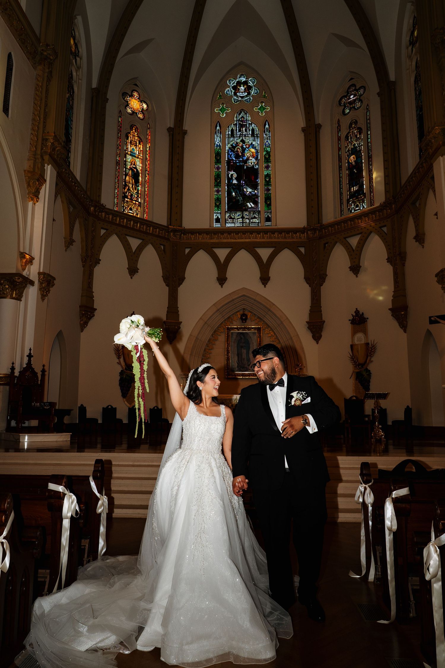 A romantic wedding ceremony takes place in a stunning Gothic cathedral with ornate stained glass windows and arched ceilings.