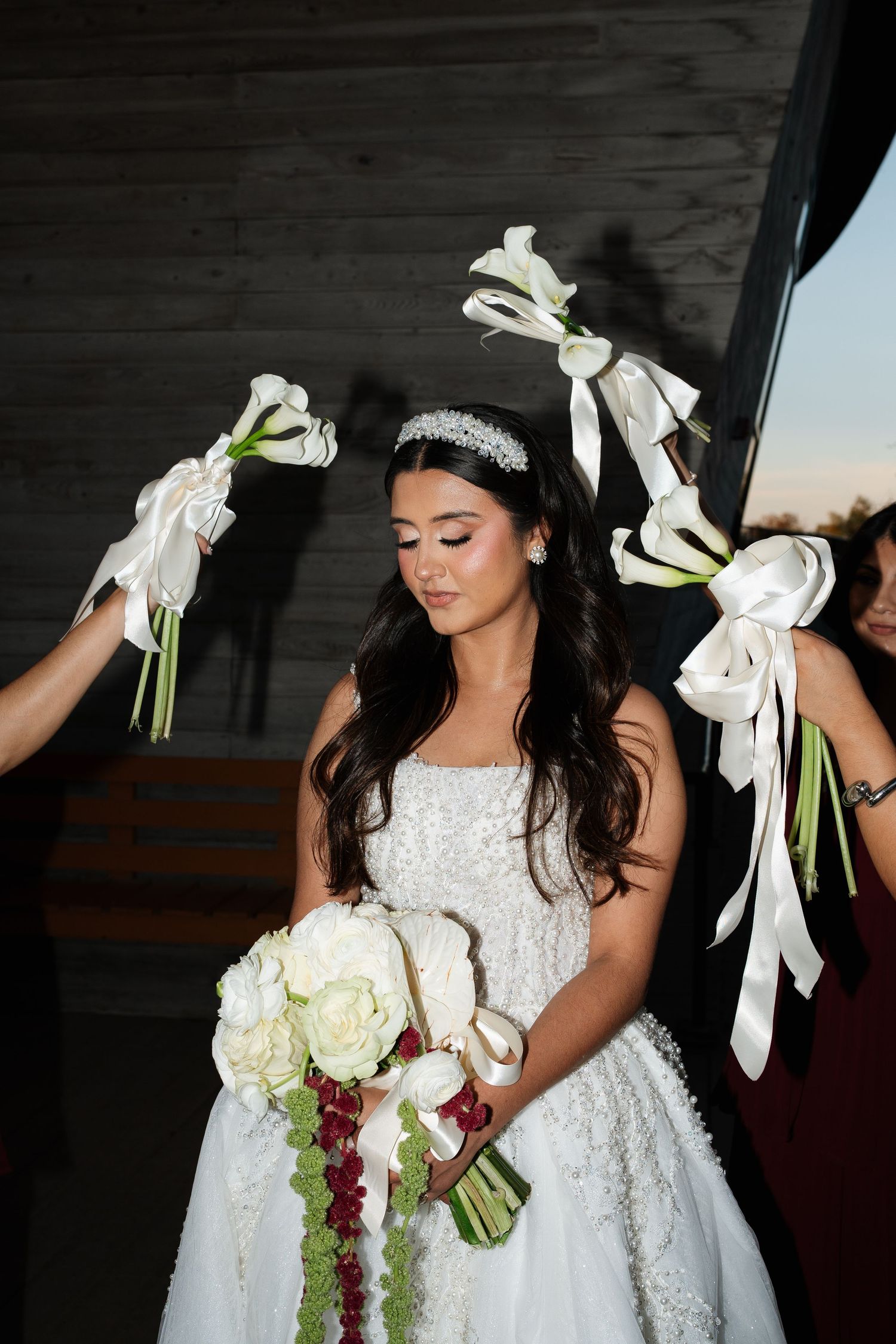A bride in a white lace gown holds flowers while others raise bouquets around her.
