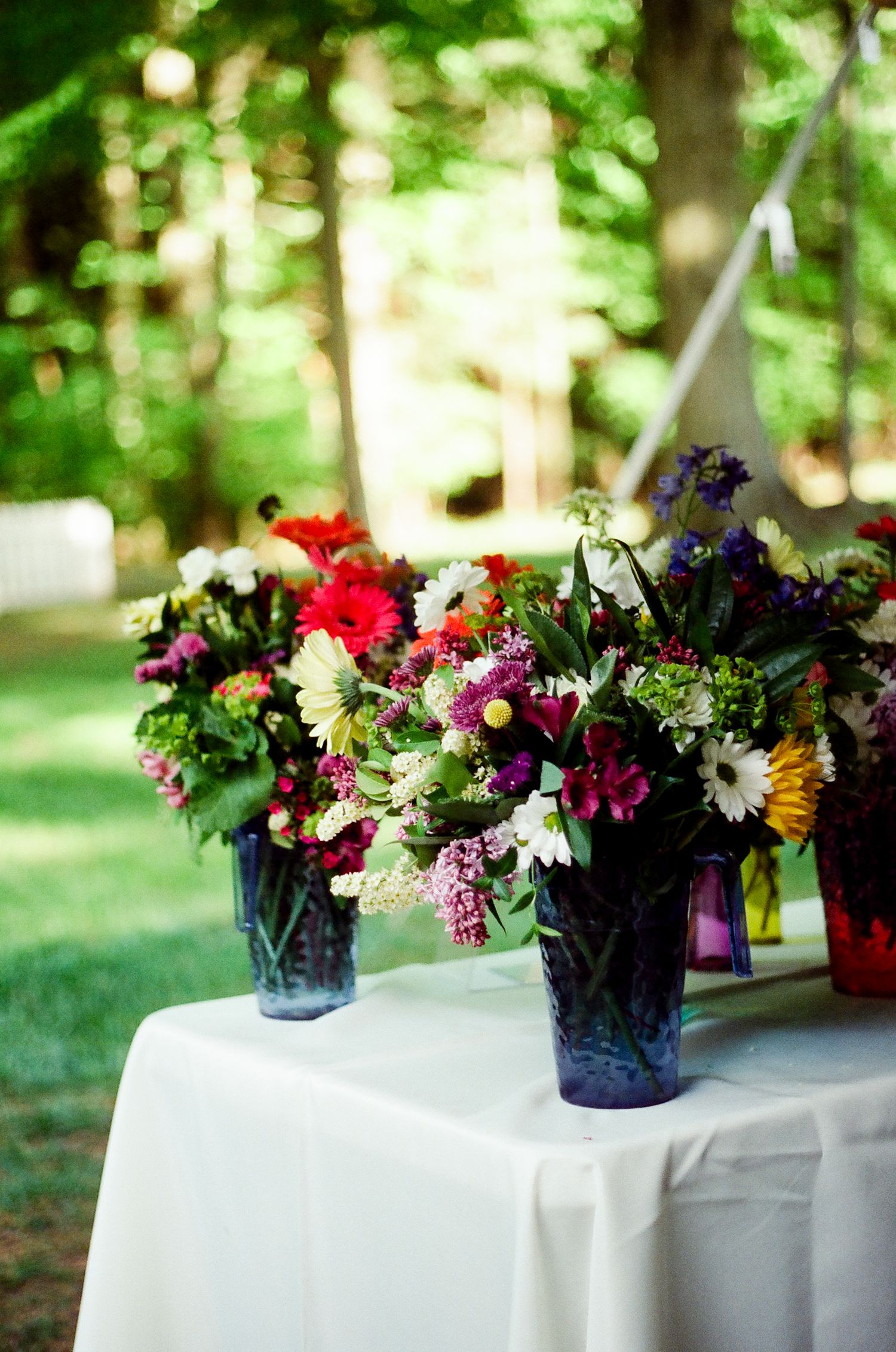 Vibrant wildflower arrangements in blue vases displayed on a white tablecloth.