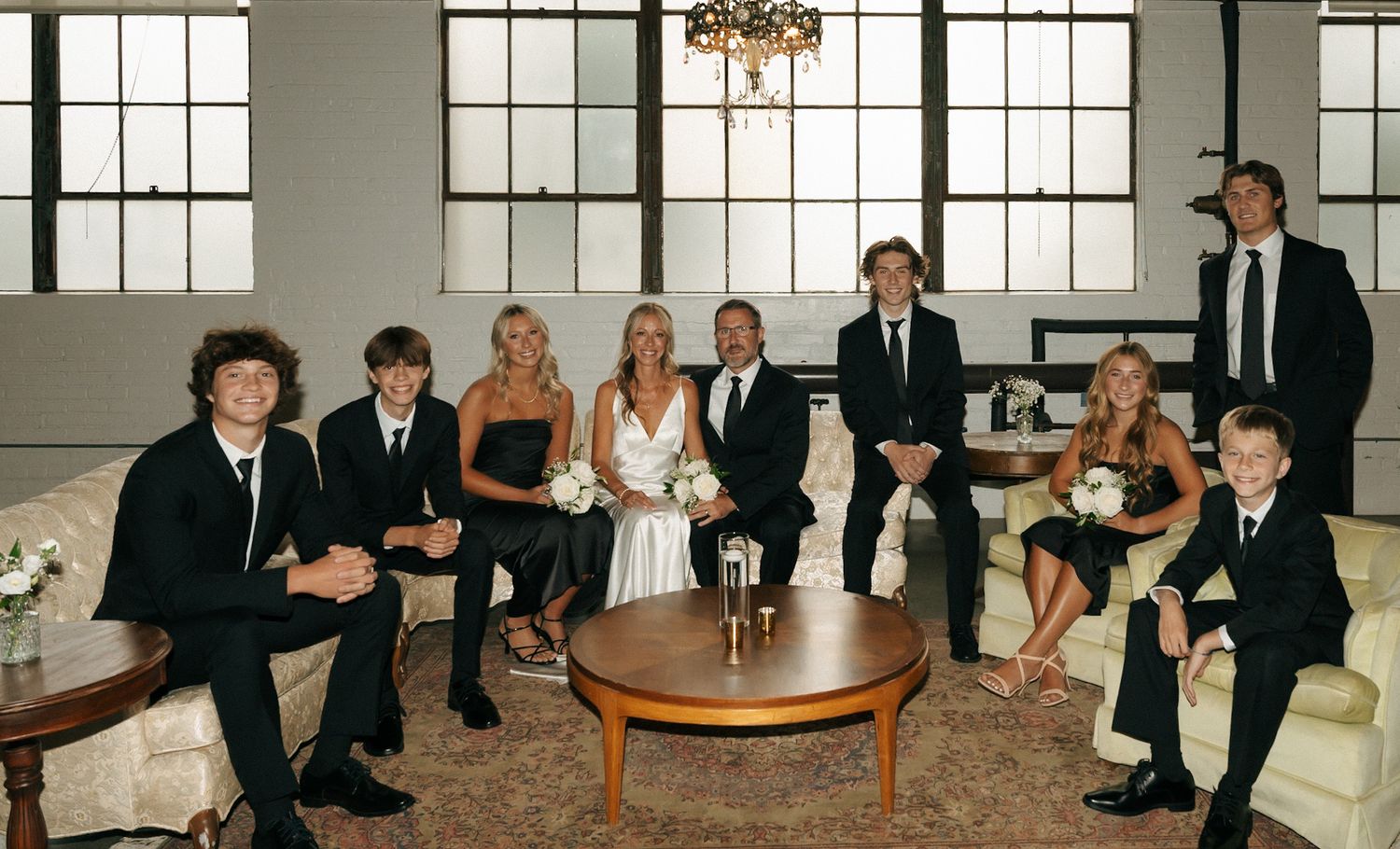 Large group seated in formal attire around tables in an elegant room with tall windows.