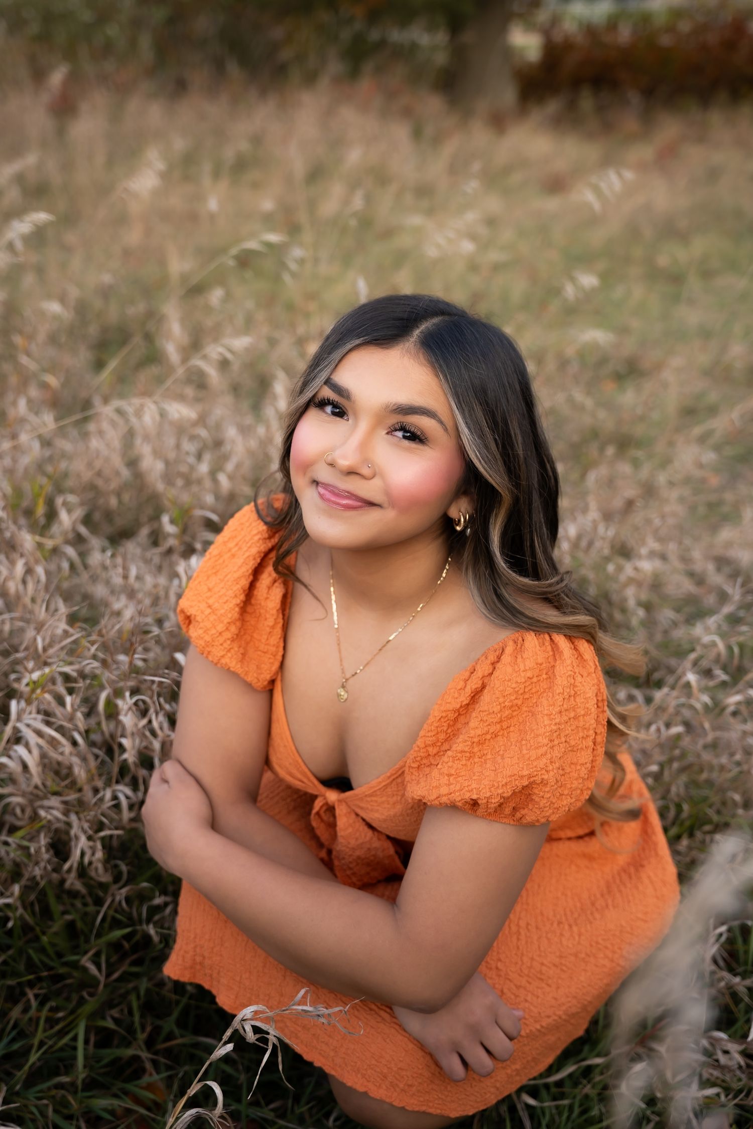 Portrait in a field wearing orange textured top with puff sleeves against natural dried grass background.