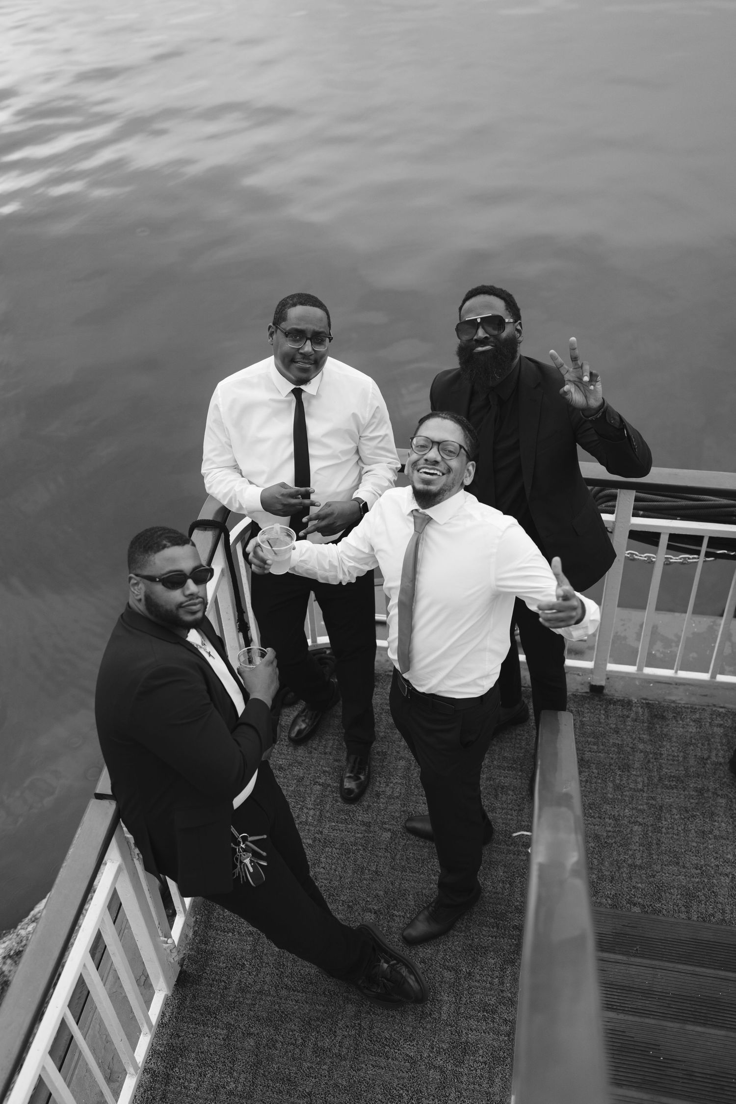 Wedding party relaxing on dock by water in formal attire.