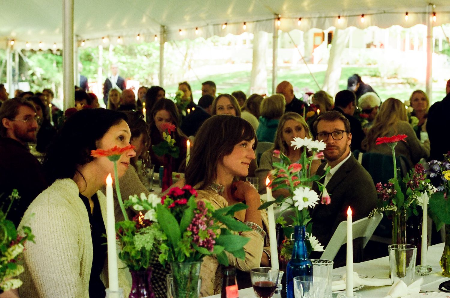 Wedding reception under a tent with string lights and floral centerpieces on dining tables.
