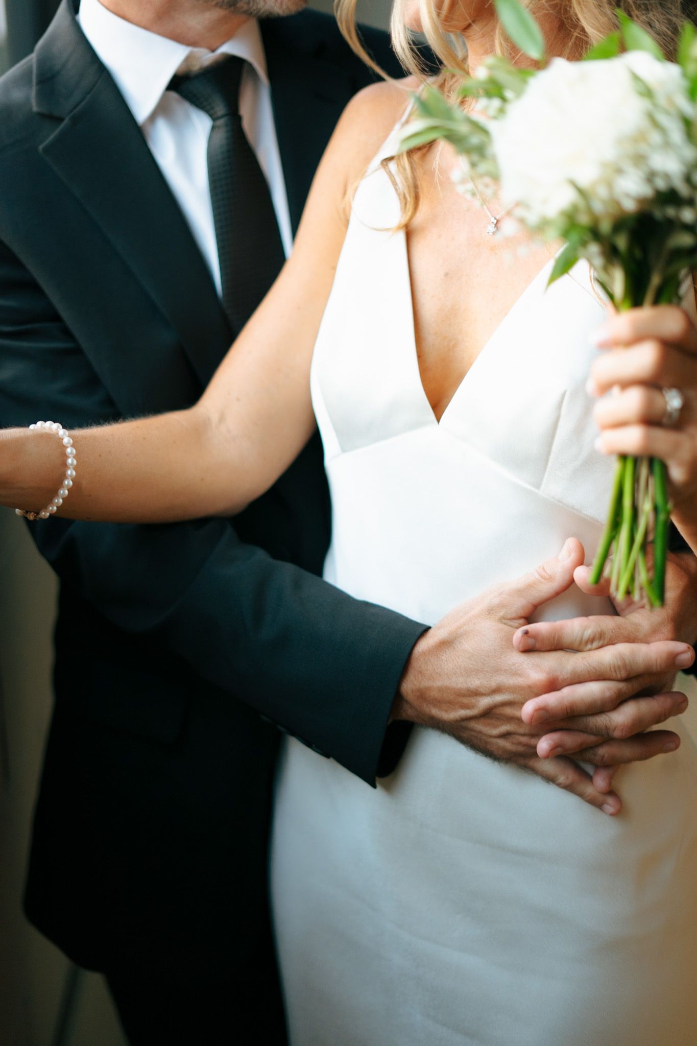 Close-up details of formal wedding attire and hands holding a bouquet.