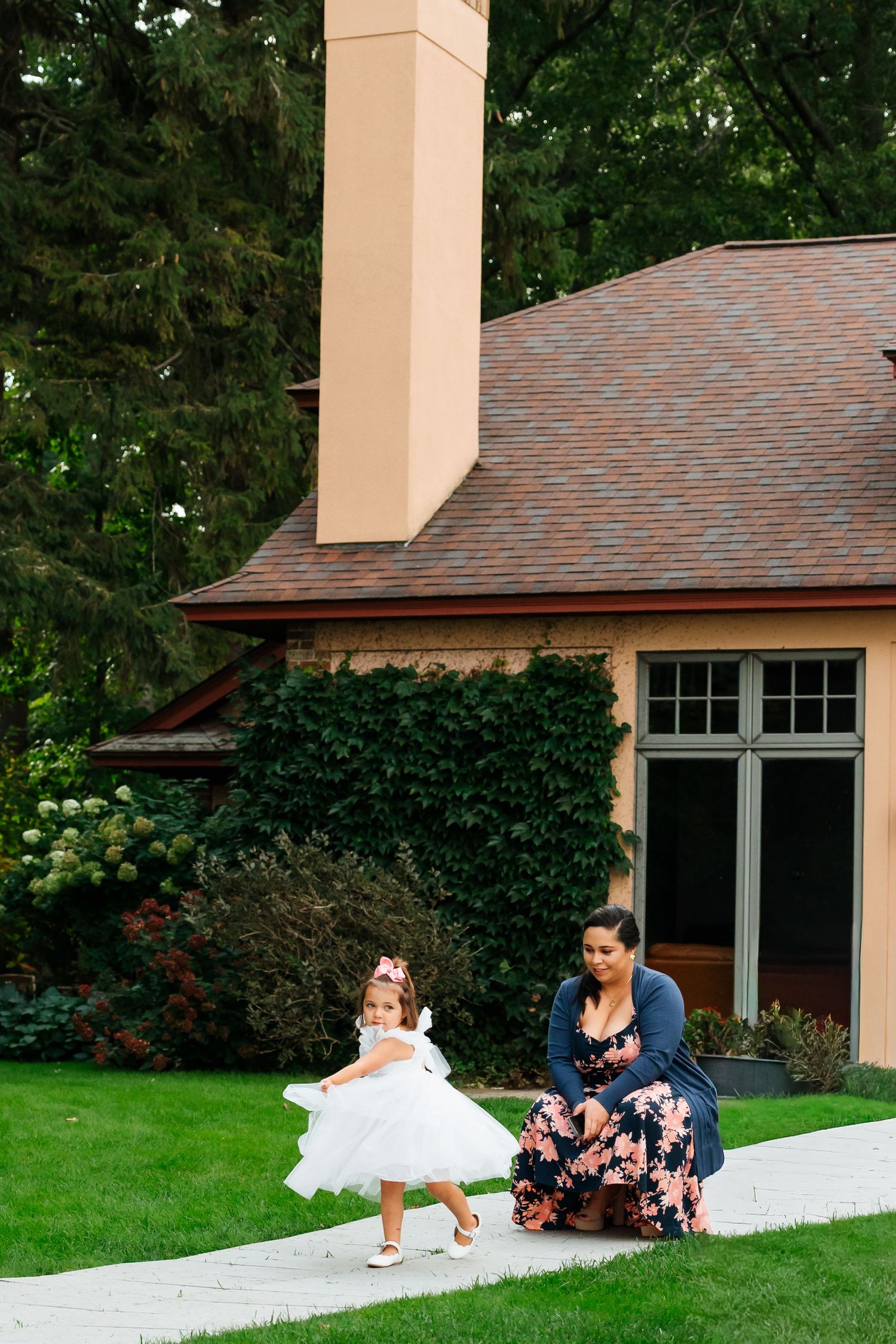 Wedding party members playfully rolling down a grassy hill outside a building.