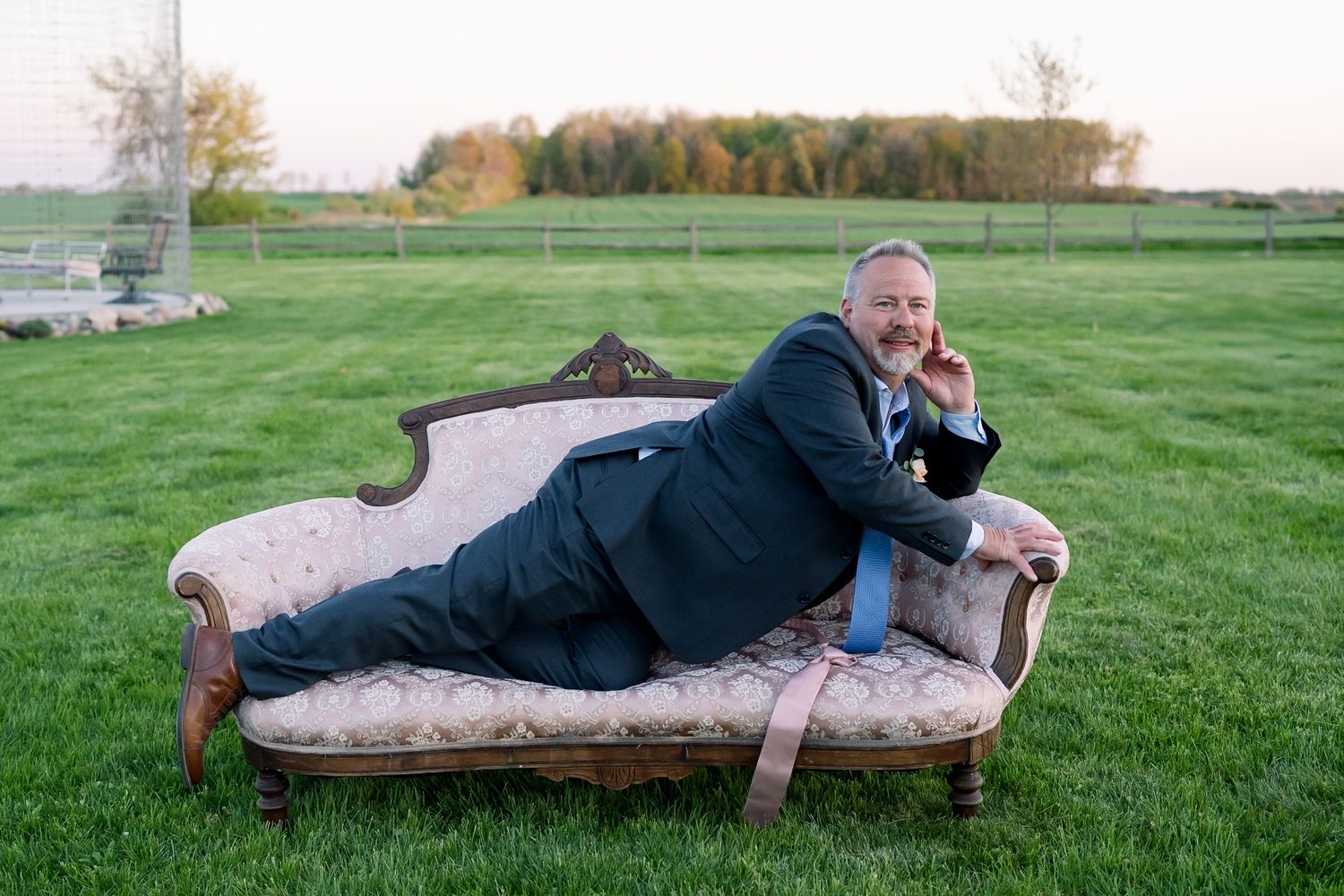 A vintage floral sofa placed in a green field serves as a unique wedding photo prop.