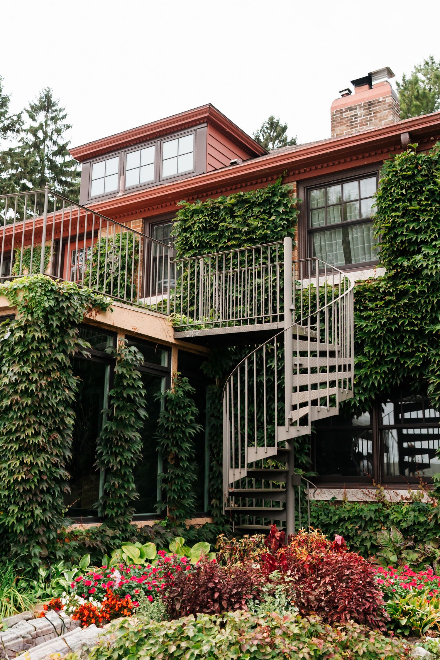 A red modern house with spiral staircase and ivy-covered walls features beautiful landscaping.
