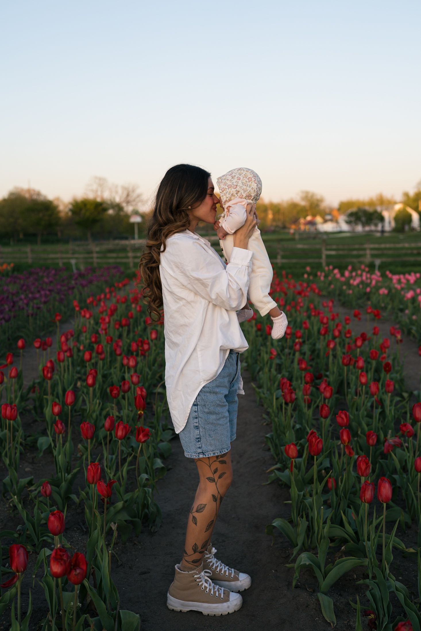 A tender moment between parent and baby in a field of red tulips at dusk.