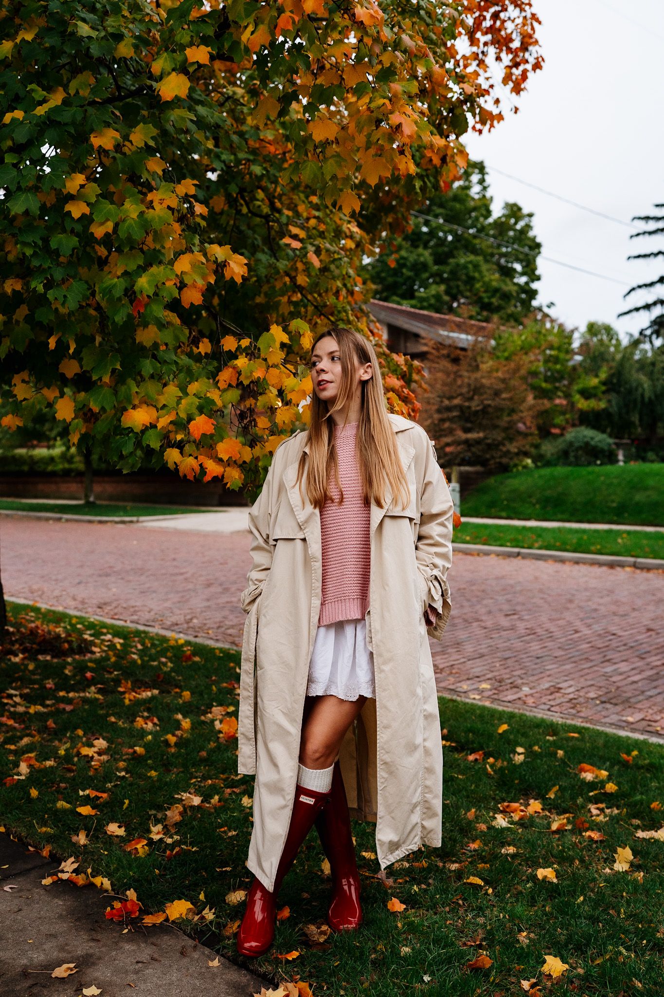Autumn fashion scene with beige trench coat and burgundy boots among fallen leaves.