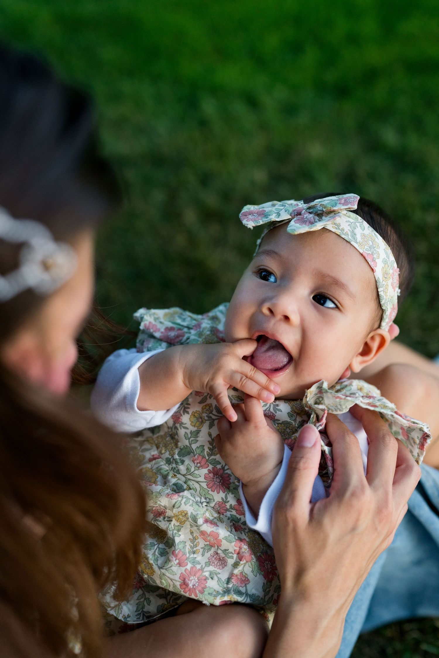Baby wearing floral headband being fed while lying down outdoors.