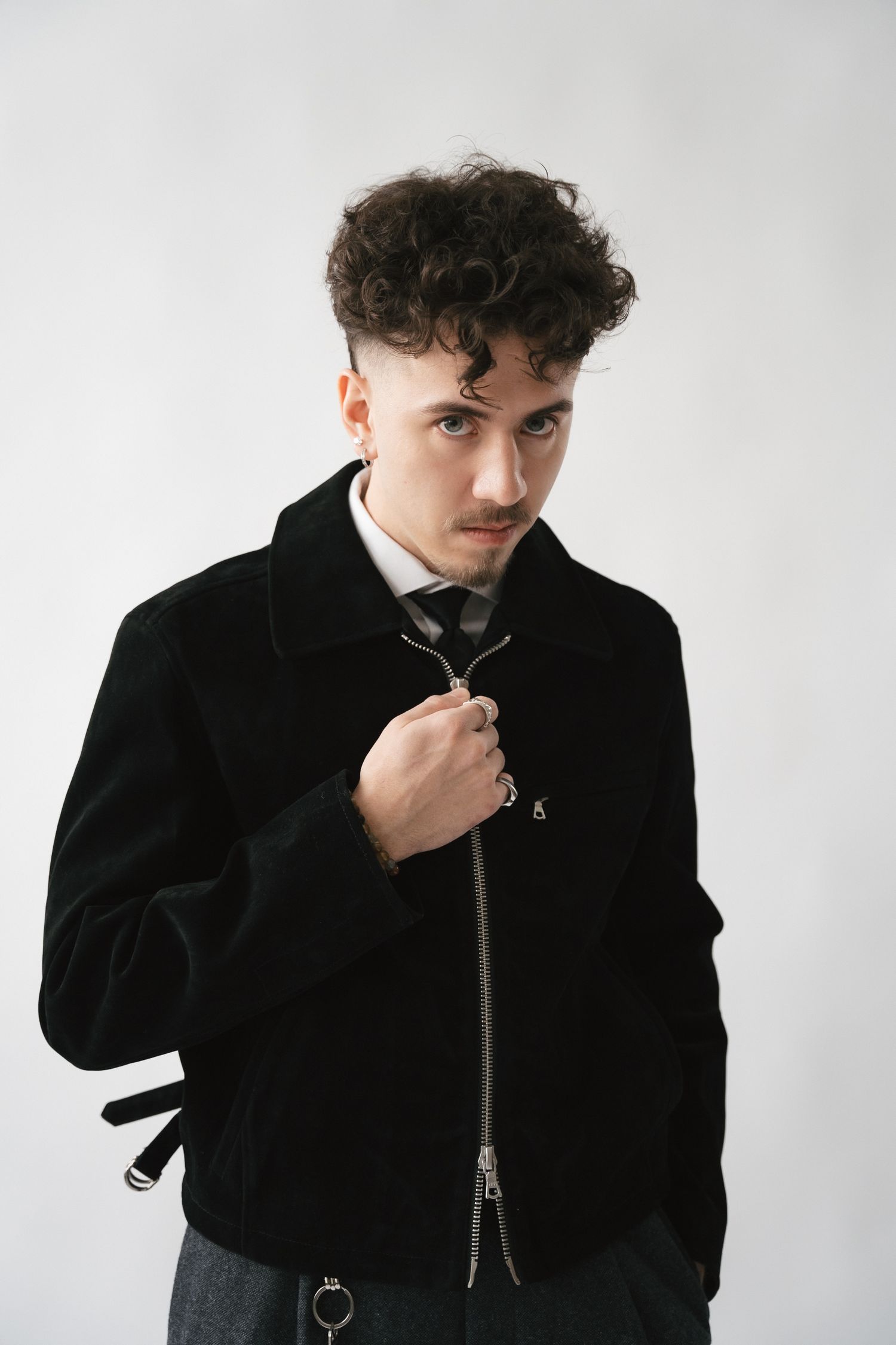 Person in black coat and turtleneck poses against white backdrop in minimalist fashion shoot.
