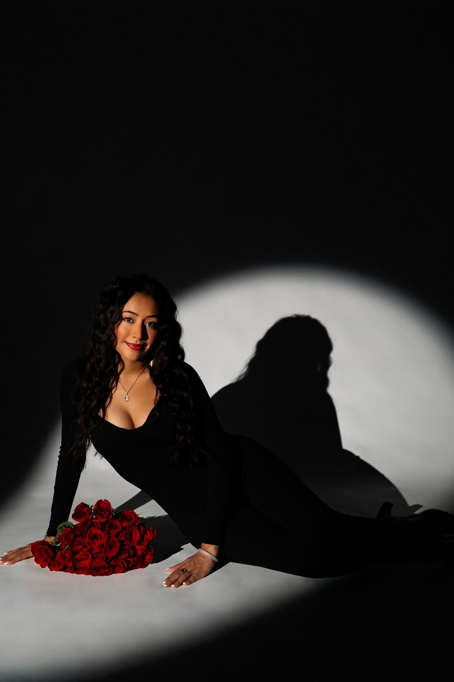 Dramatic studio photo with red roses and figure in black against dark background.